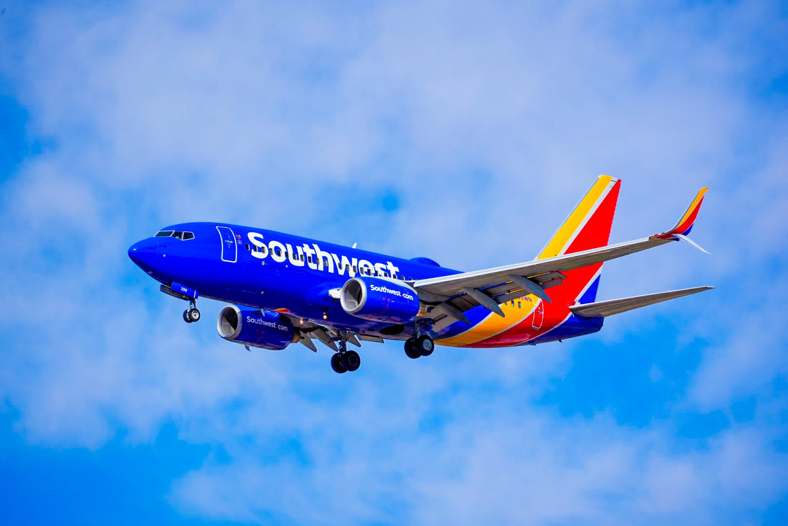 A Southwest Airlines airplane flying in the sky with a blue sky and clouds background.