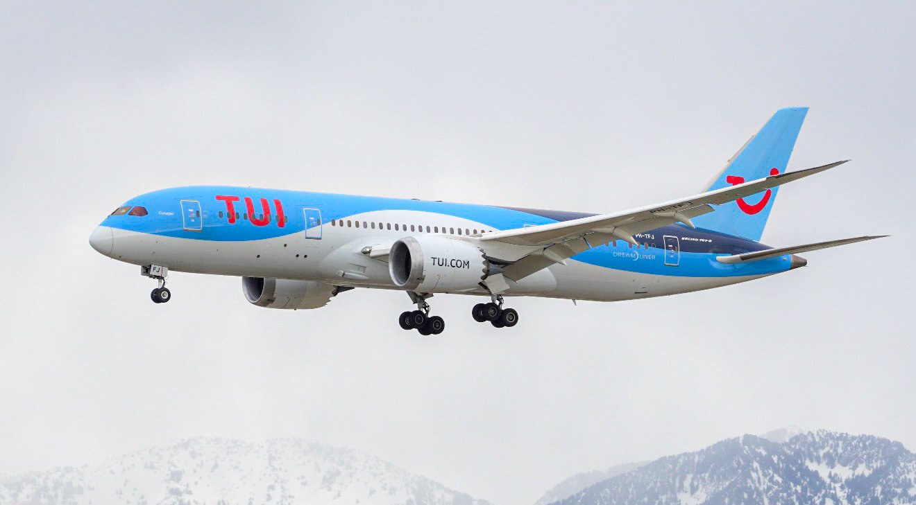 A TUI airplane flying in the sky over snow-covered mountains.