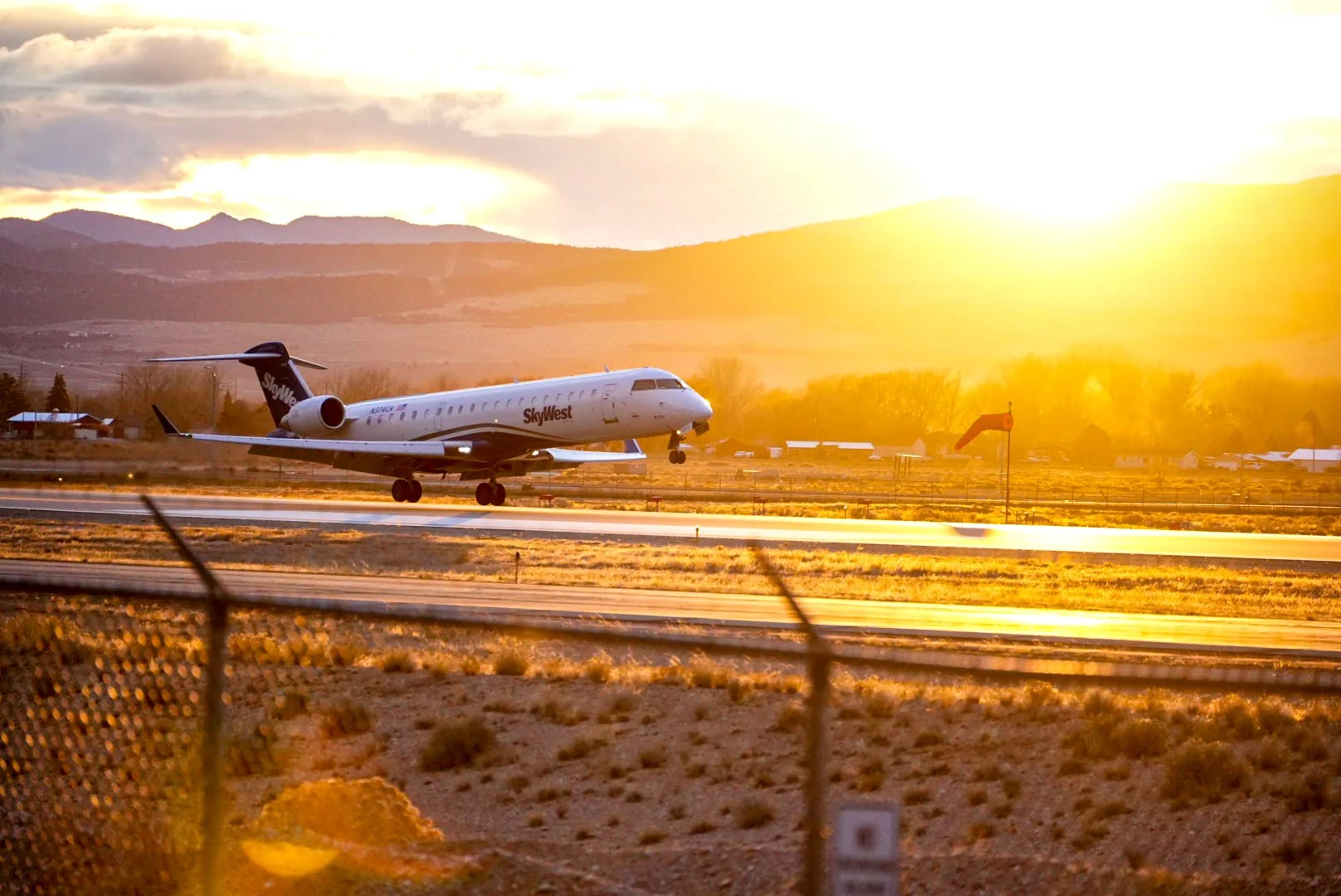 An airplane taking off from an airport runway during sunset, with mountains and trees in the background.