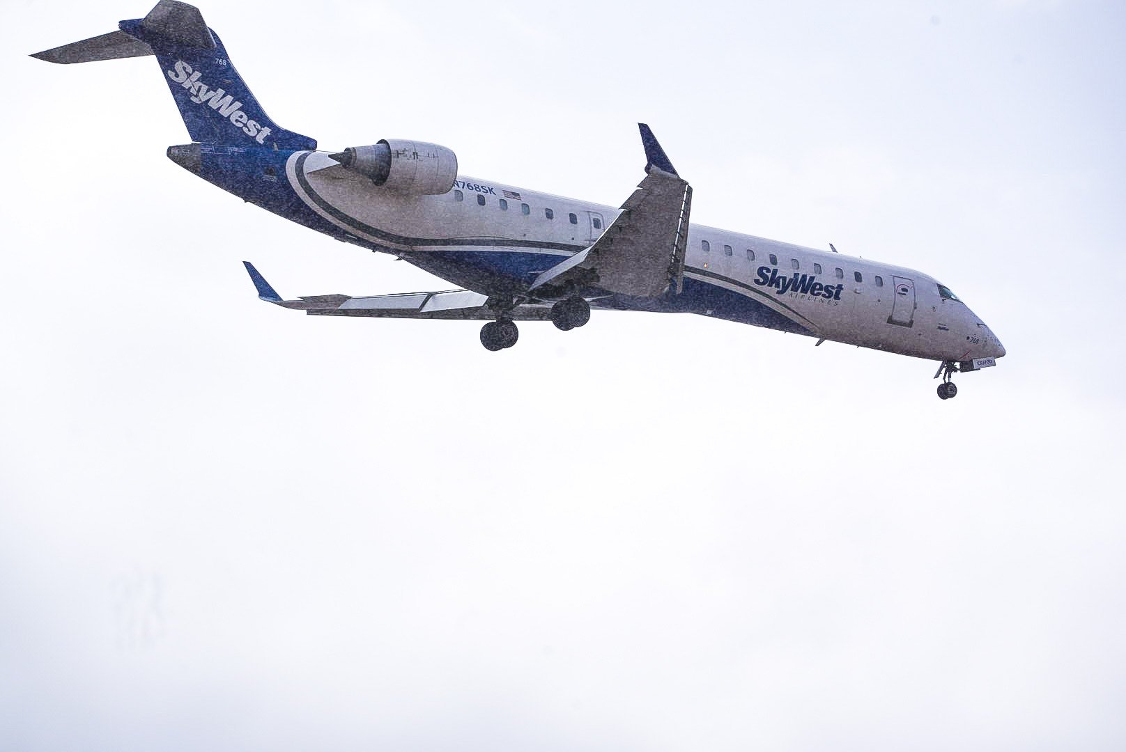 An airplane from SkyWest Airlines flying in cloudy weather with its landing gear extended.