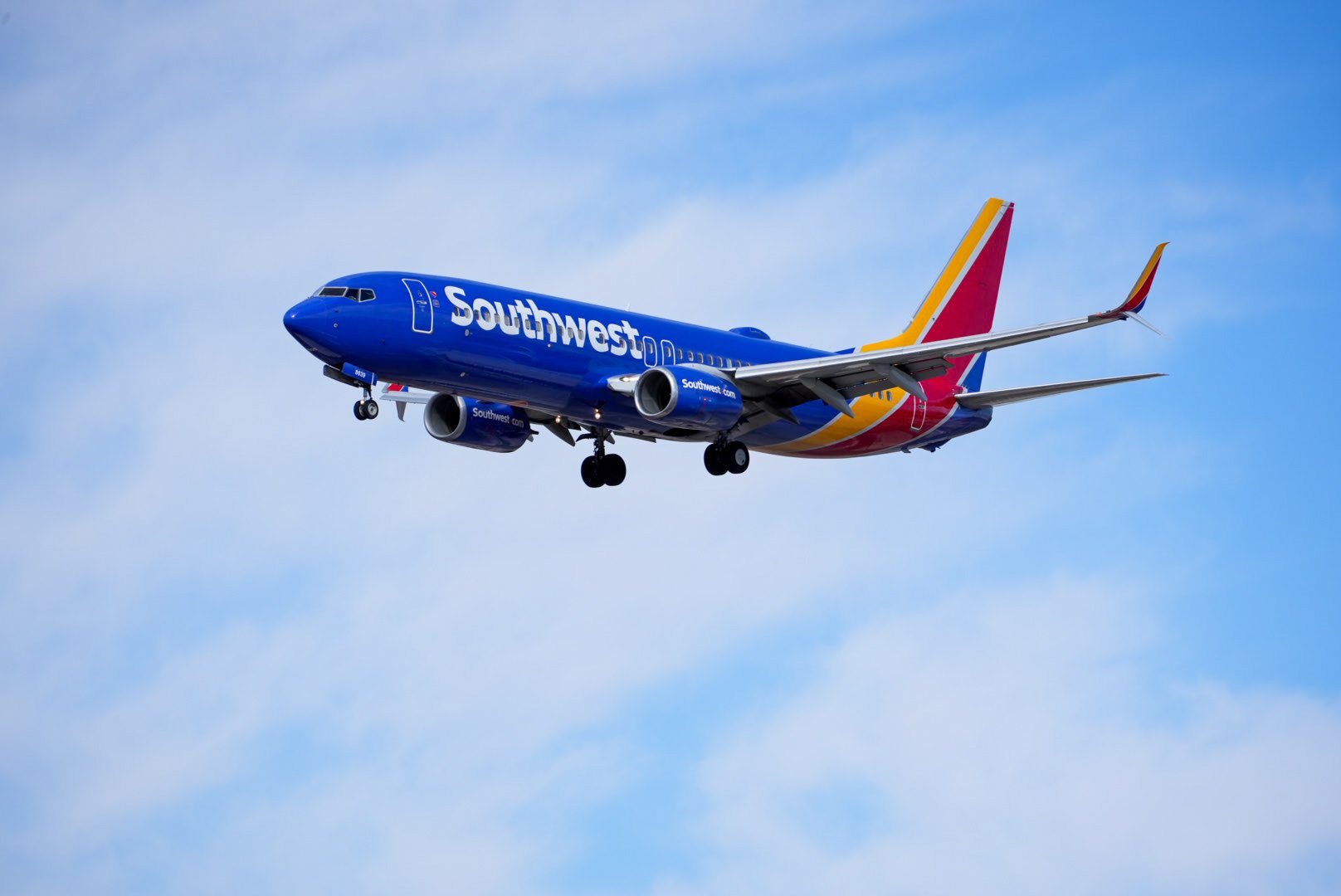 A Southwest Airlines airplane flying in the sky with blue sky and scattered clouds.