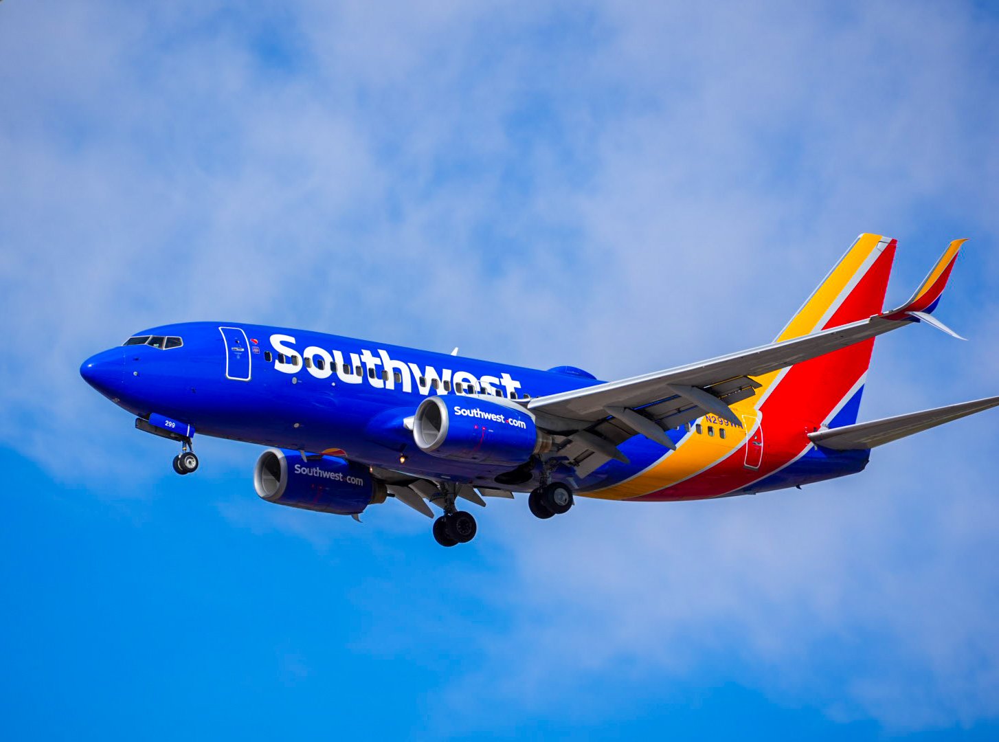 A Southwest Airlines airplane in flight with a blue body and a multicolored tail against a partly cloudy blue sky.