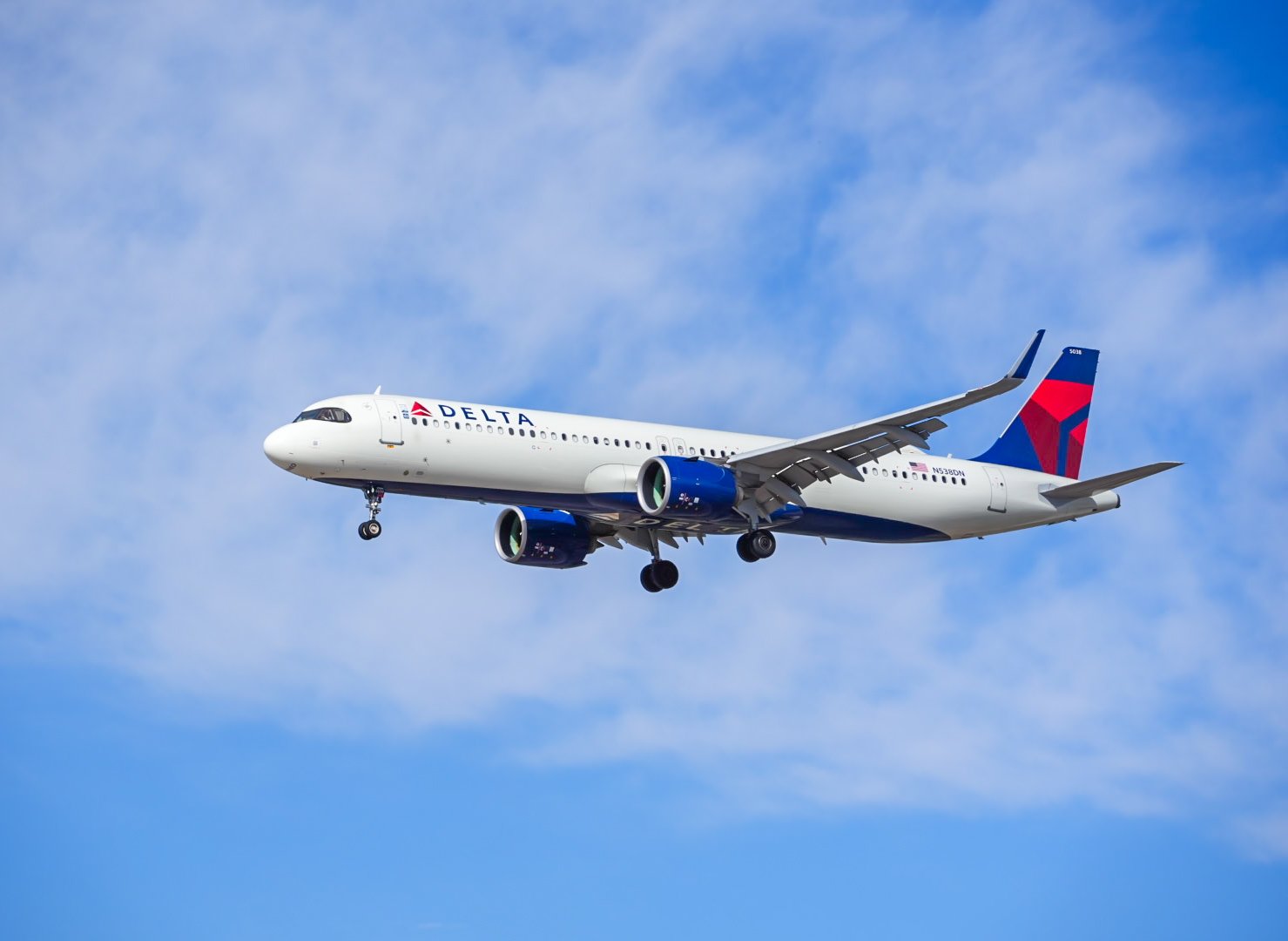 Delta Airlines airplane flying in a blue sky with some clouds.