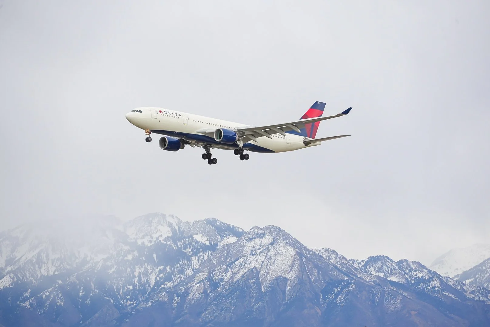A Delta airplane flying in the sky above snow-capped mountains.