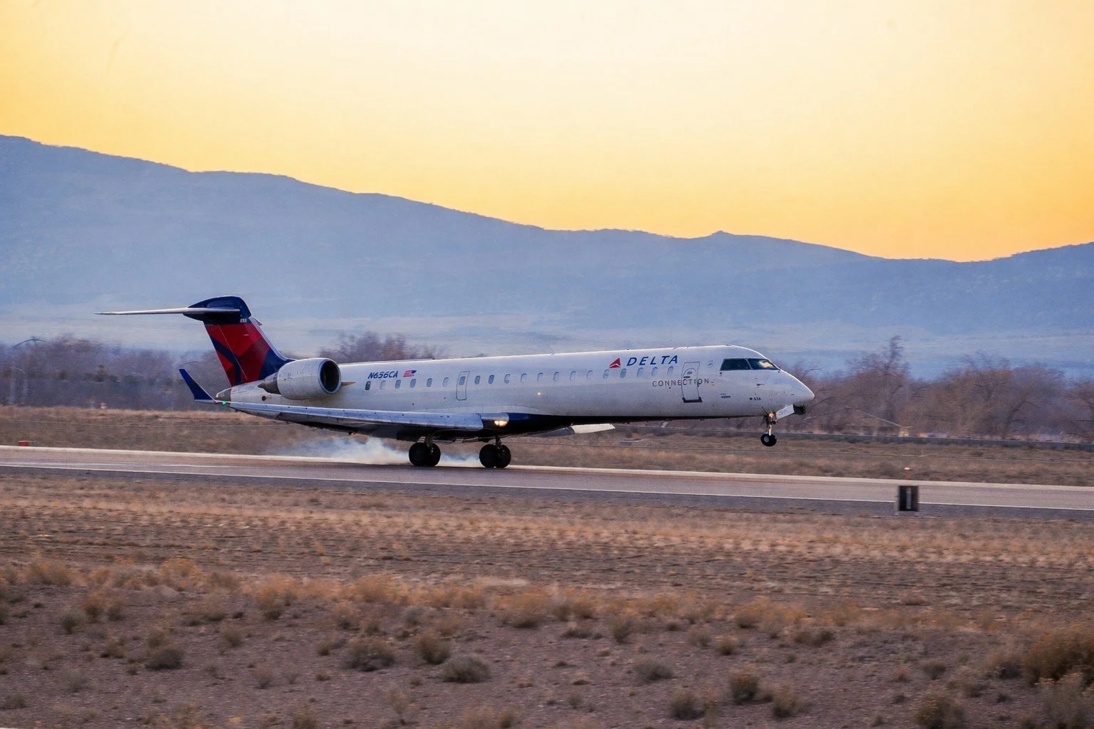 A Delta Connection regional jet taking off from a runway at sunset with mountains in the background.