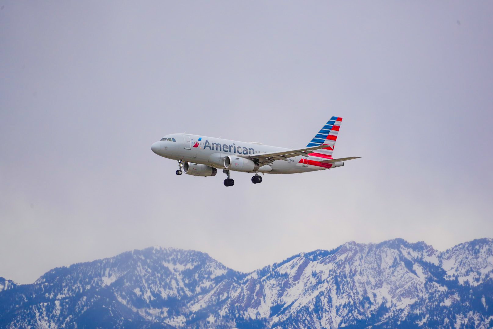 An American Airlines airplane flying over snow-capped mountains.