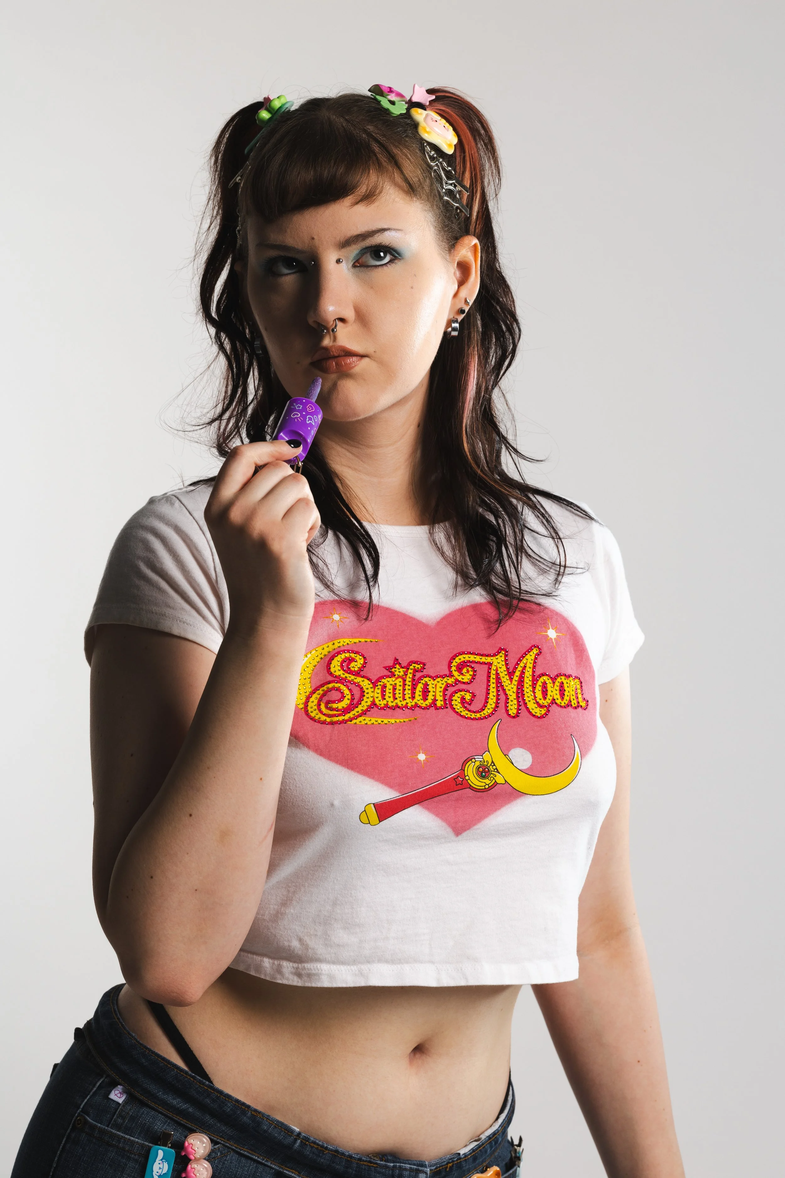 A woman with tattoos and piercings wearing a Sailor Moon t-shirt, holding a purple toy with a straw.