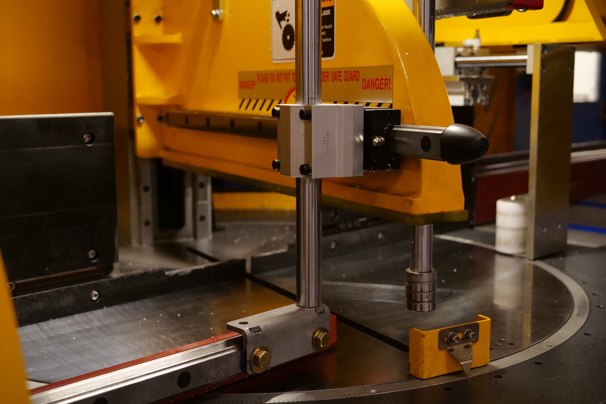 Close-up of a yellow industrial machine part with metal rods, bolts, and safety warning labels.