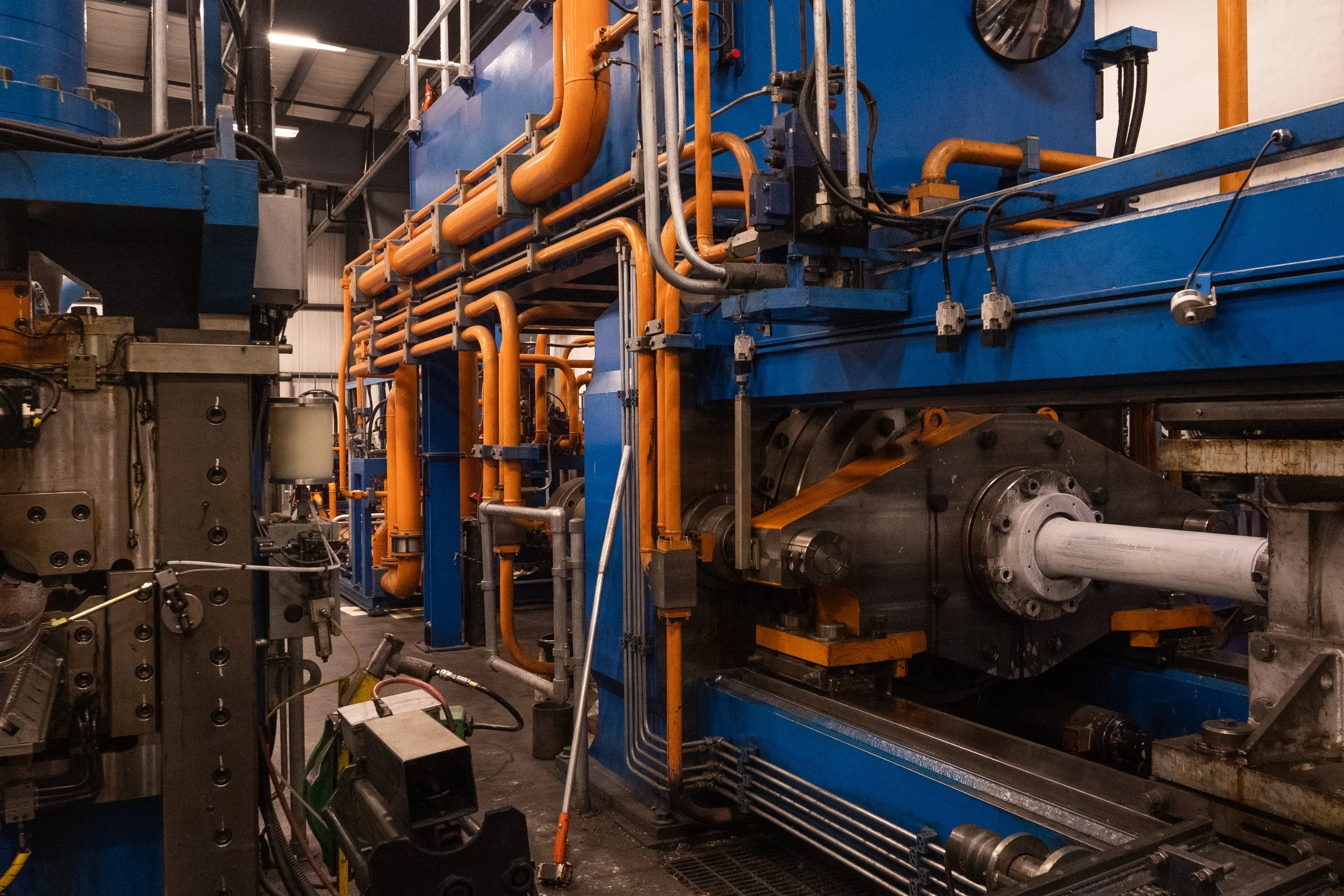 Industrial machinery with orange pipes and blue panels inside a factory or manufacturing plant.