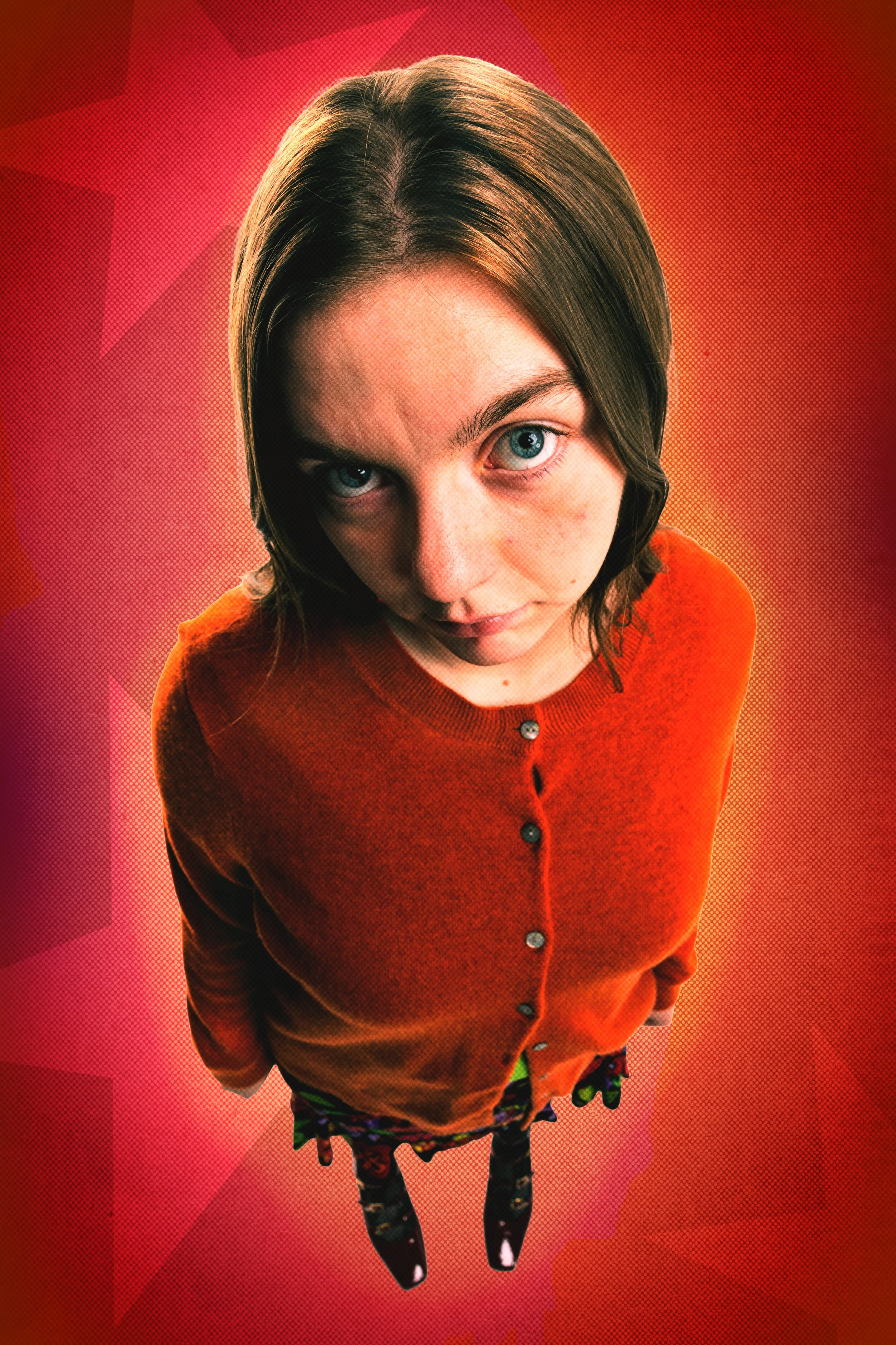 A young girl with blue eyes and shoulder-length brown hair, wearing an orange sweater and patterned tights, looking up at the camera against a red background.
