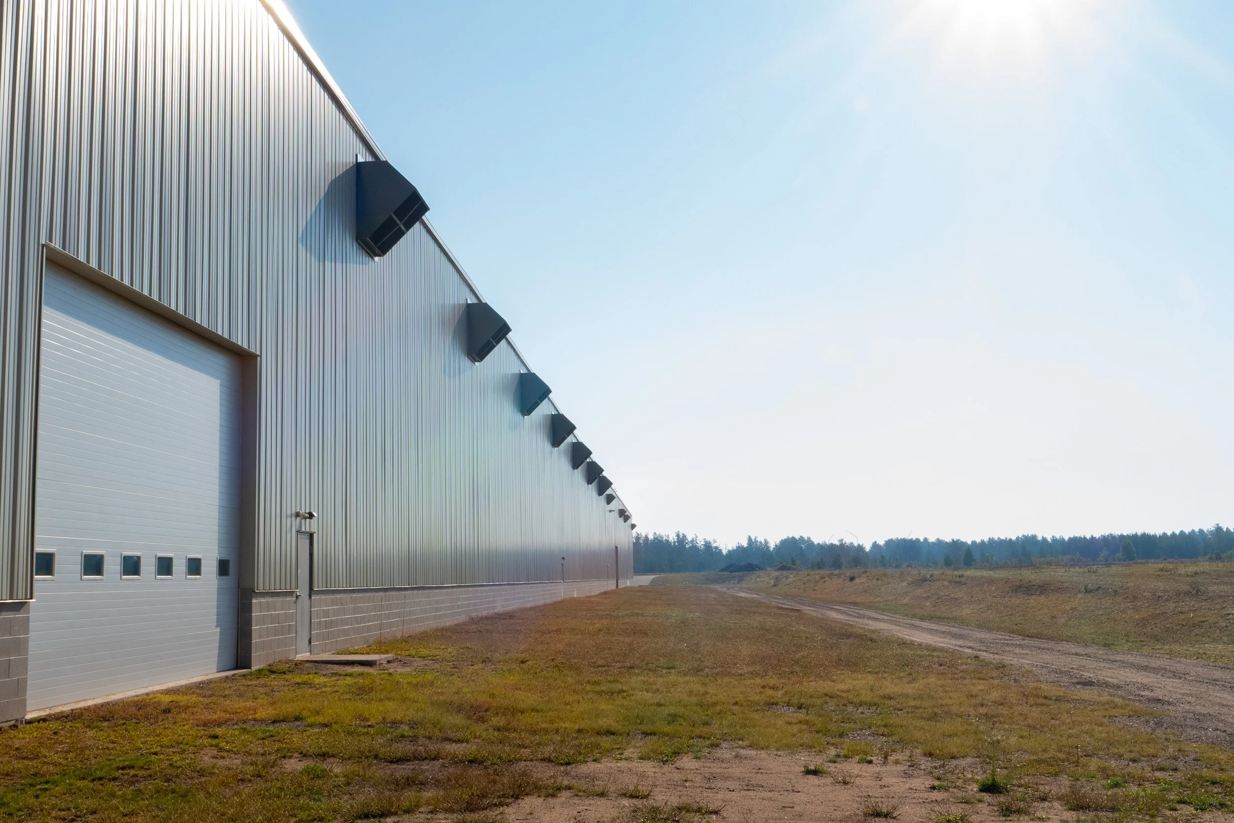 A large industrial warehouse building with multiple loading bays and black exterior lights on a clear, sunny day.