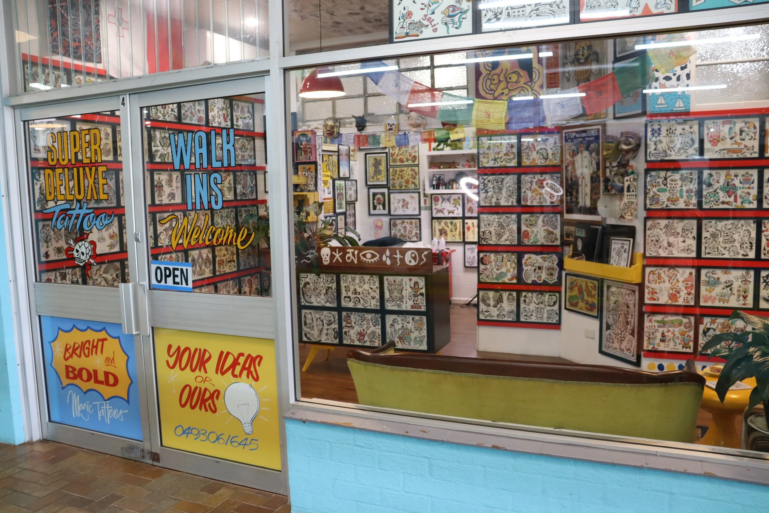Tattoo shop window with colorful signs and displays of tattoo flash art inside.