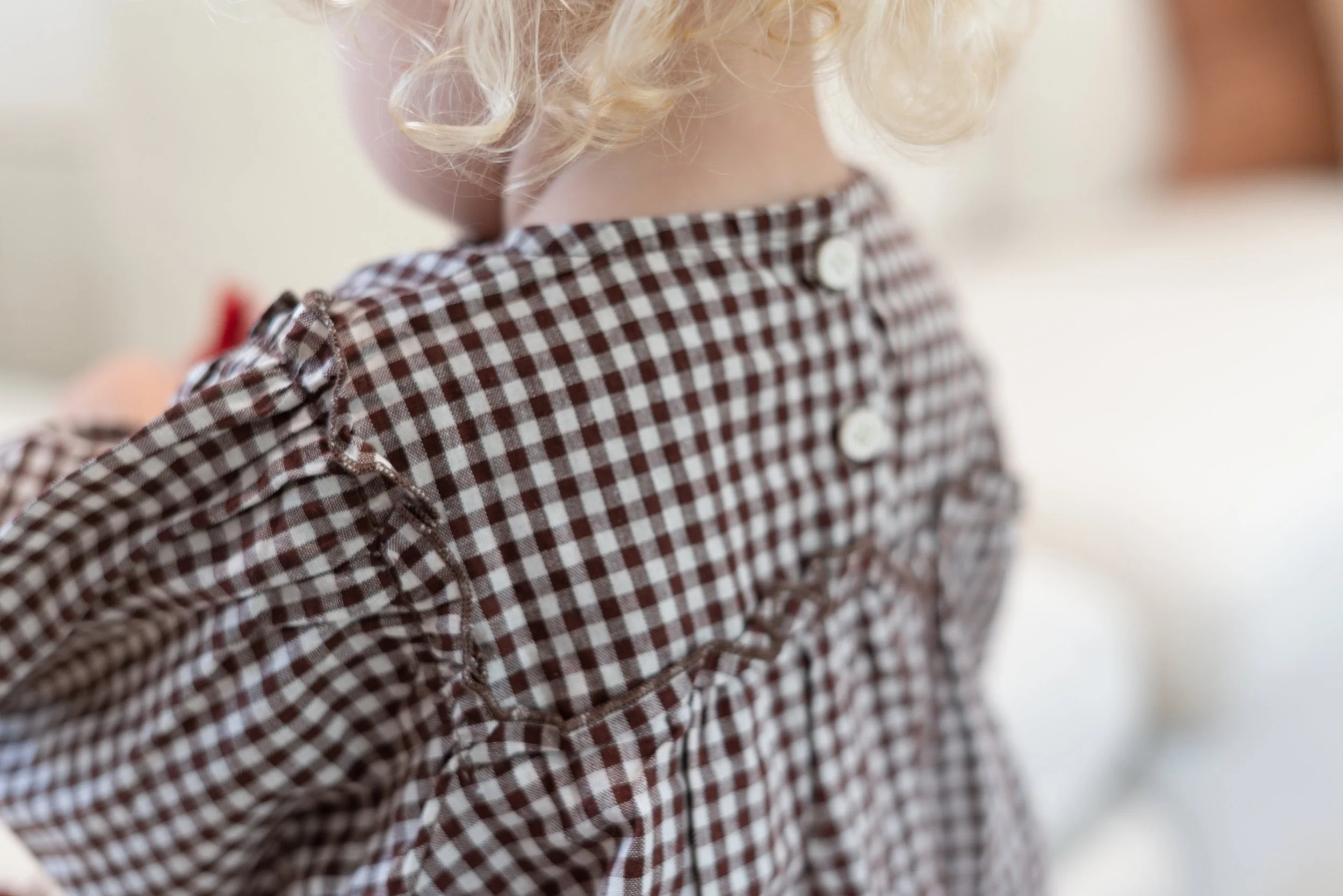 Close-up of a young girl wearing a brown and white checkered dress with ruffled shoulders and white buttons on the back.