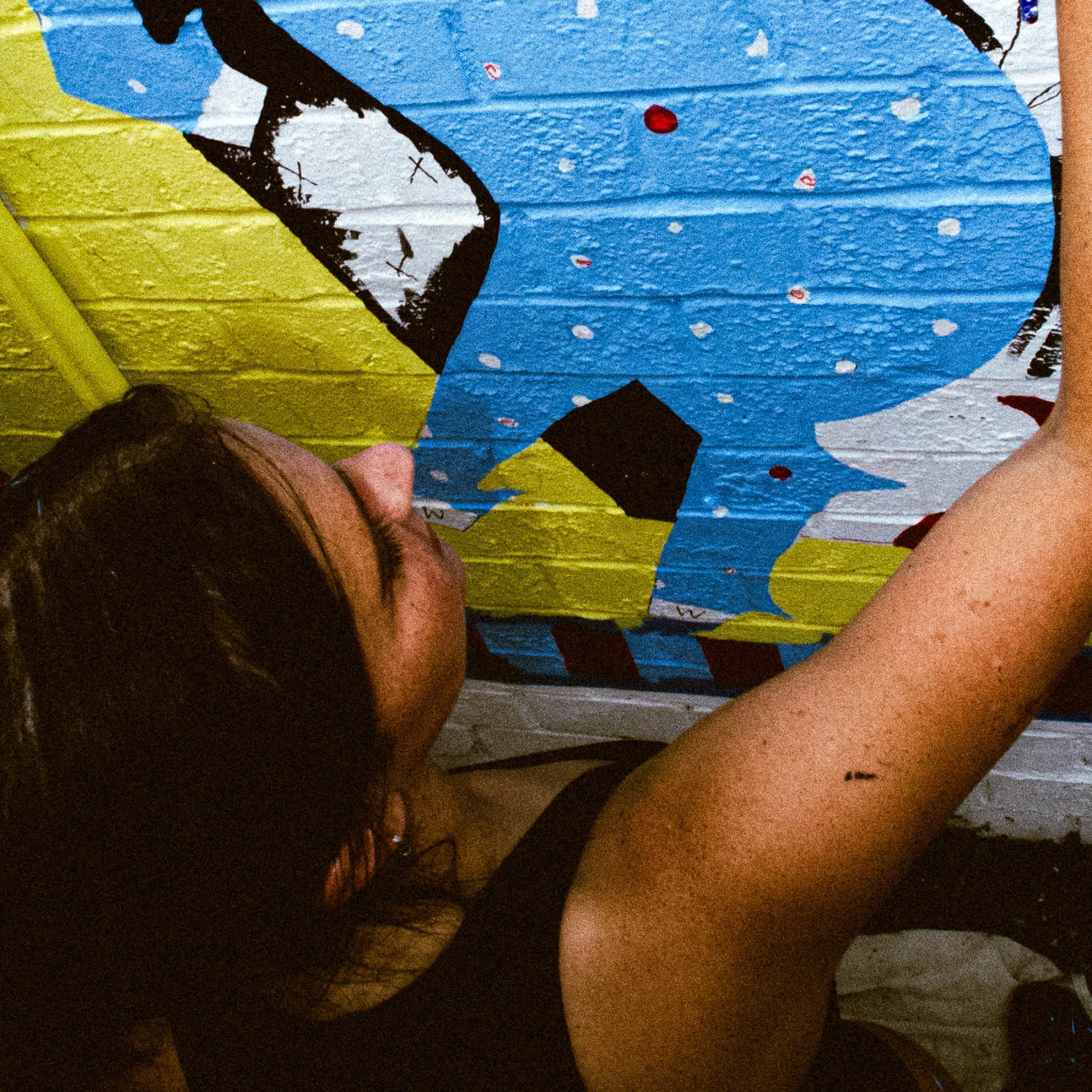 A woman painting or creating art on a colorful mural featuring a cartoon character with blue, white, black, and yellow colors.