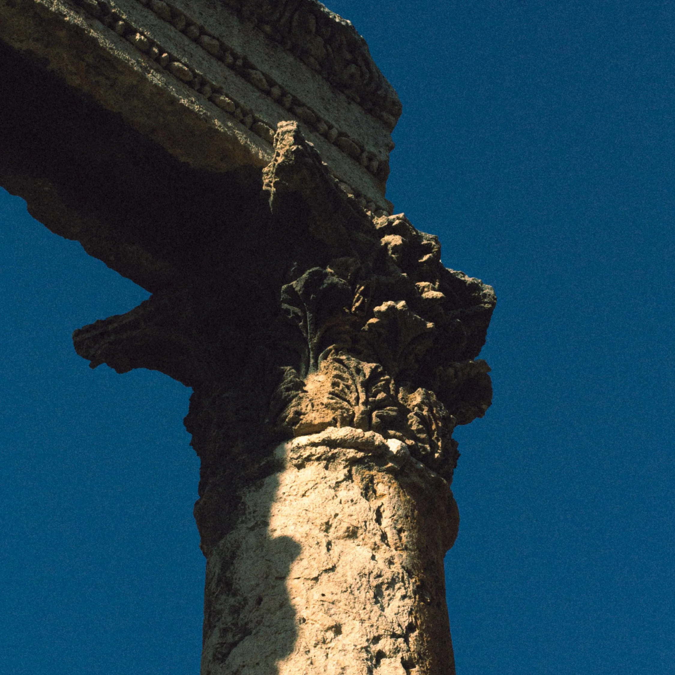 Close-up view of an ancient stone column with intricate carvings, partially shaded, against a clear blue sky.
