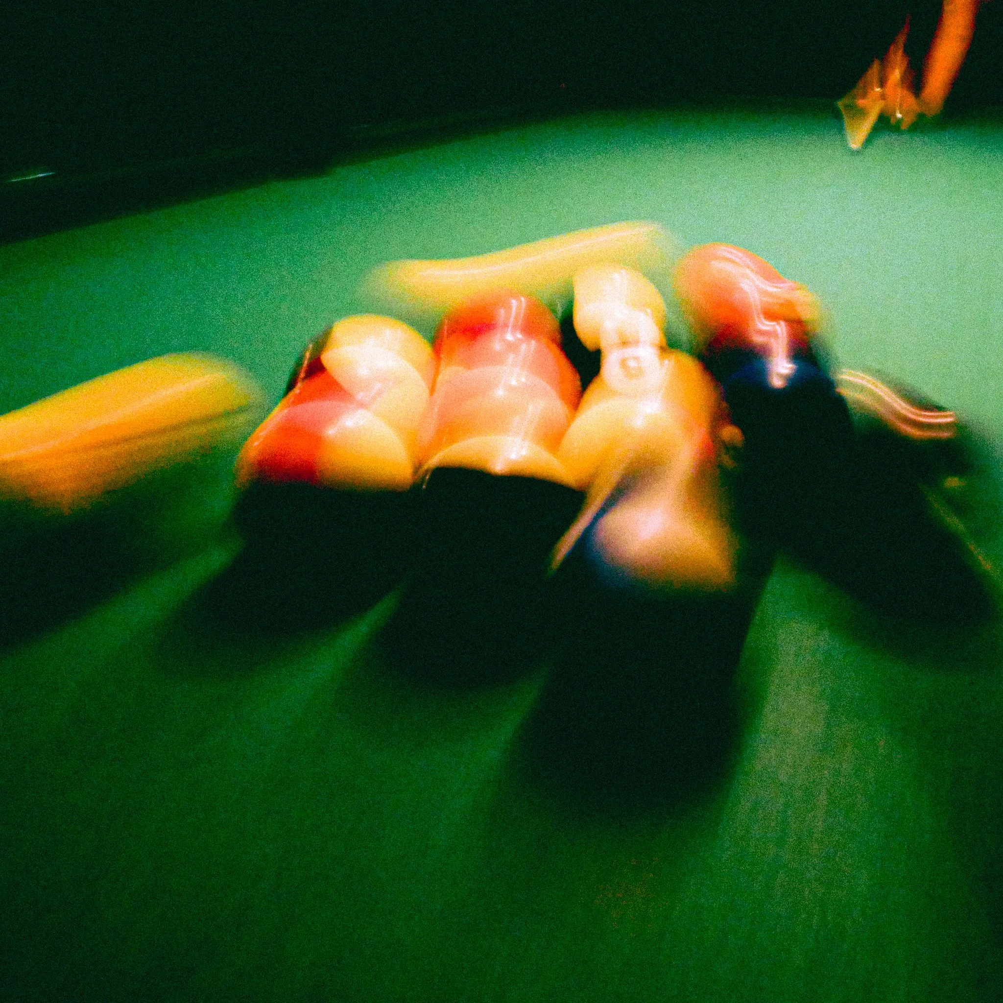 Blurred image of six red and white pool balls on a green billiards table, with yellow and orange pool cues in the background.