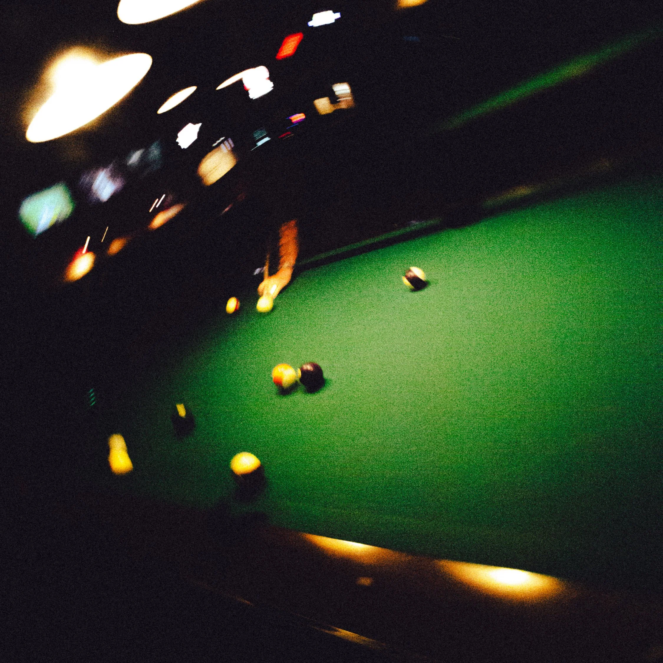 A pool table with several billiard balls scattered on the green felt, illuminated by overhead lights in a dimly lit room.