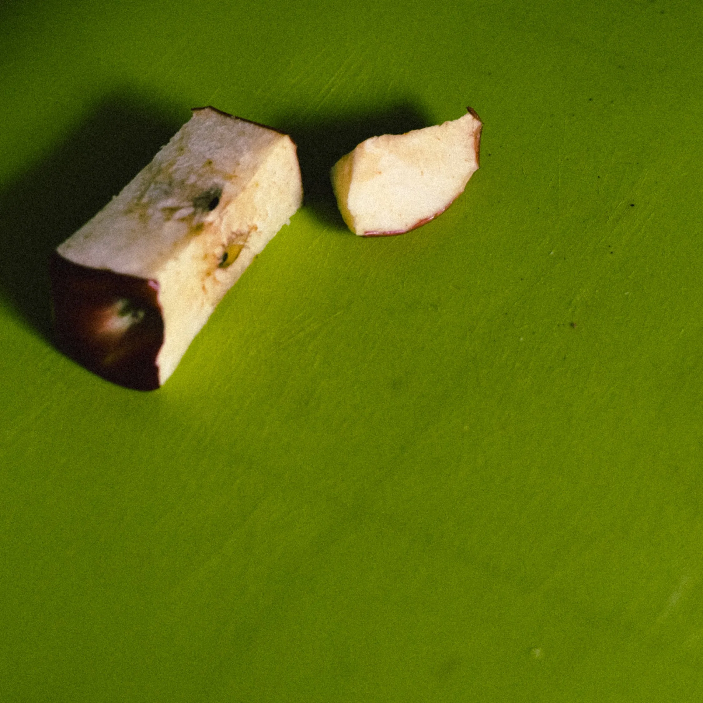 A partially eaten apple with a bite taken out of it, resting on a bright green surface.