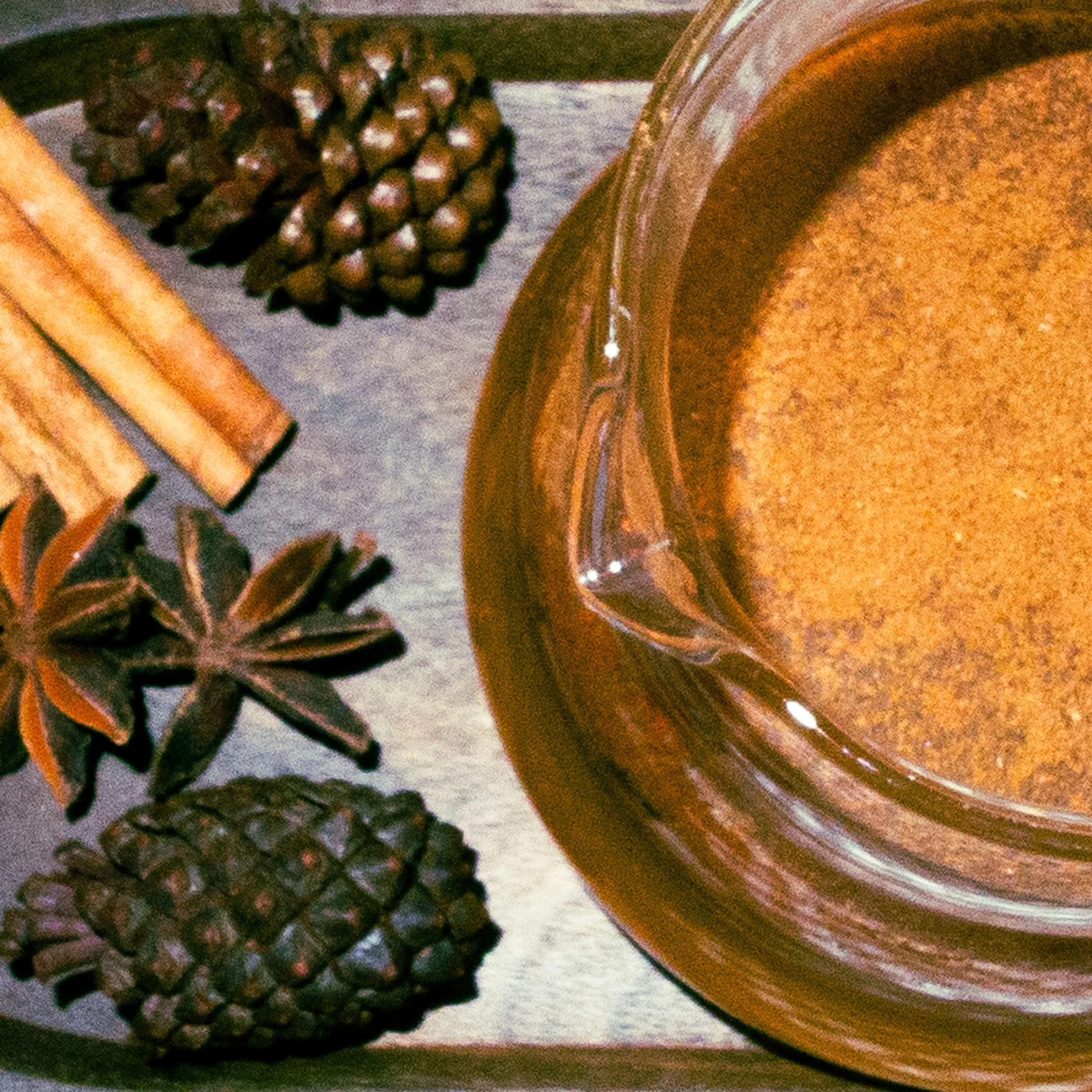 Cinnamon sticks, pinecones, star anise, and a jar of cinnamon powder on a wooden surface.