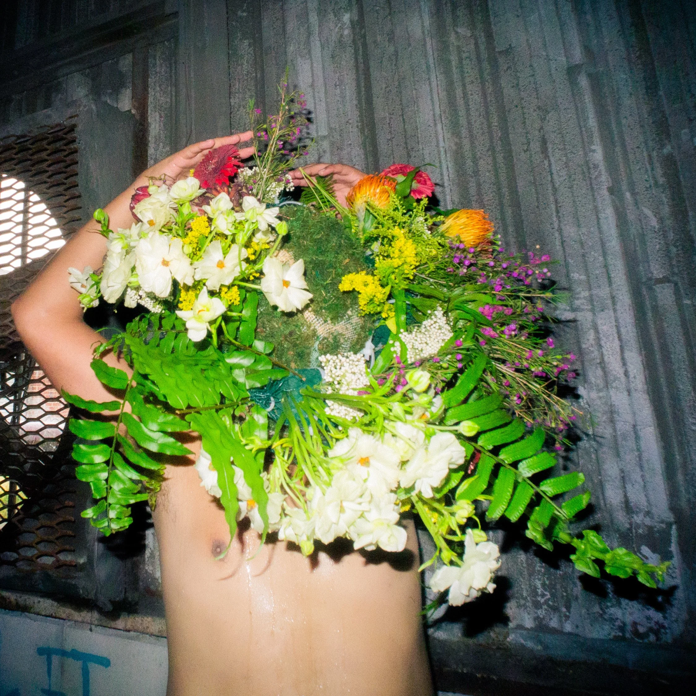 Person holding a large bouquet of mixed colorful flowers with green foliage, against a dark textured background.