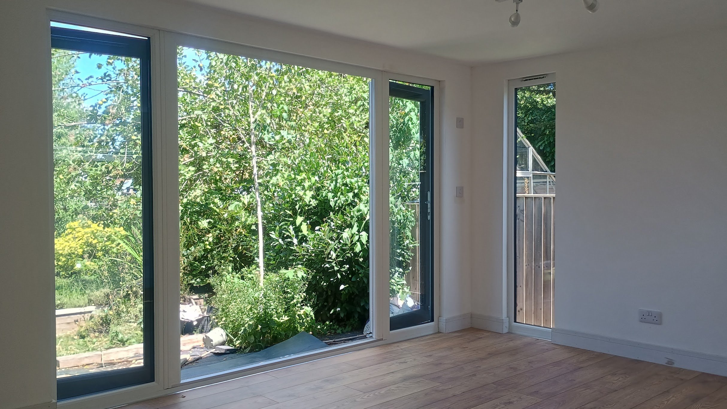 Empty room with large glass sliding doors and windows overlooking a garden with greenery and trees outside.