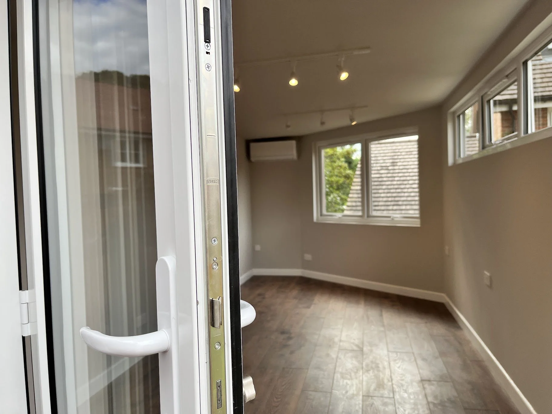 Empty room with brown wooden floor, gray walls, and multiple windows; door open showing the interior.
