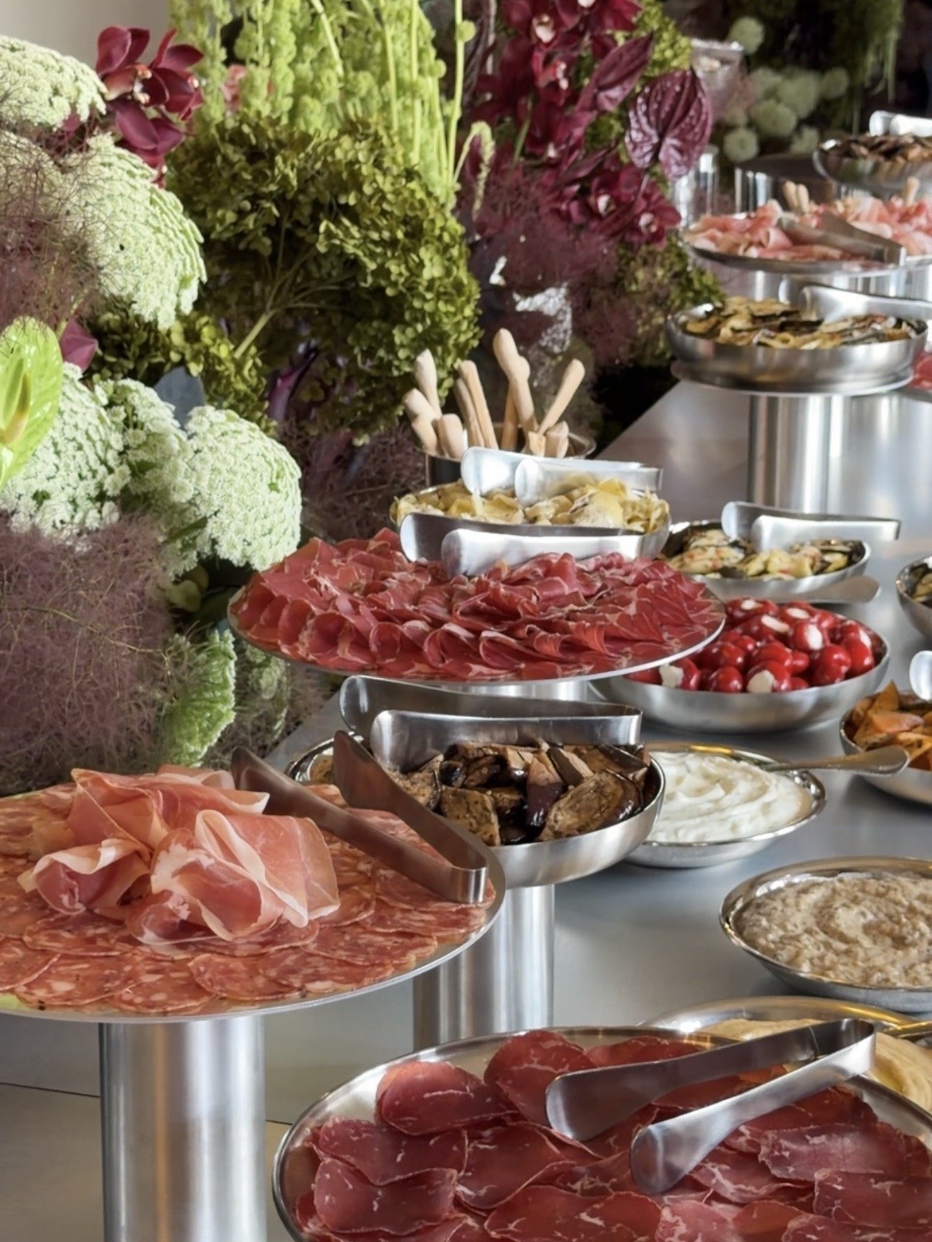 A buffet table with assorted meats, cheeses, vegetables, and dips, decorated with green and purple floral arrangements.