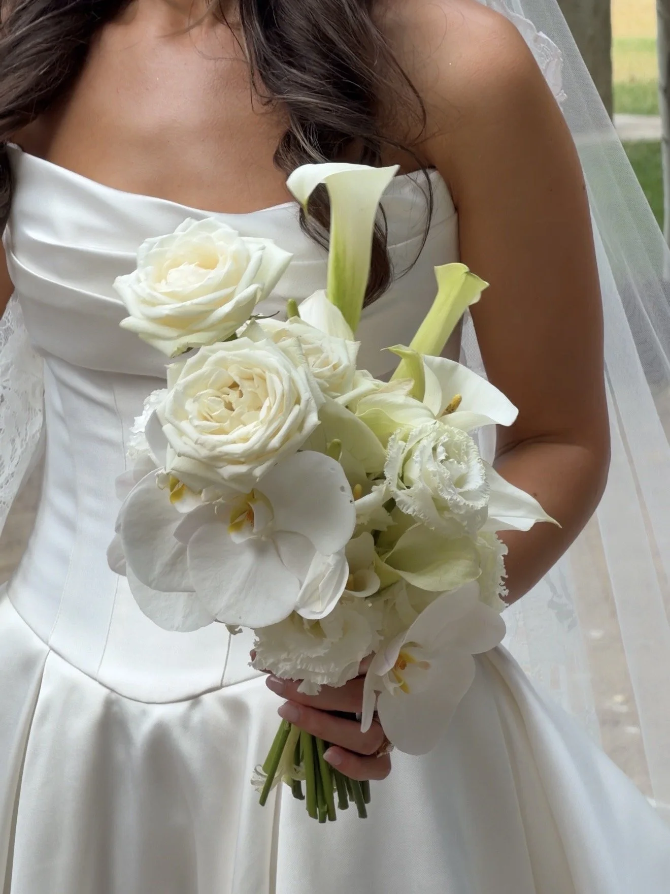 A bride in a white wedding dress holding a bouquet of white roses, calla lilies, and orchids.