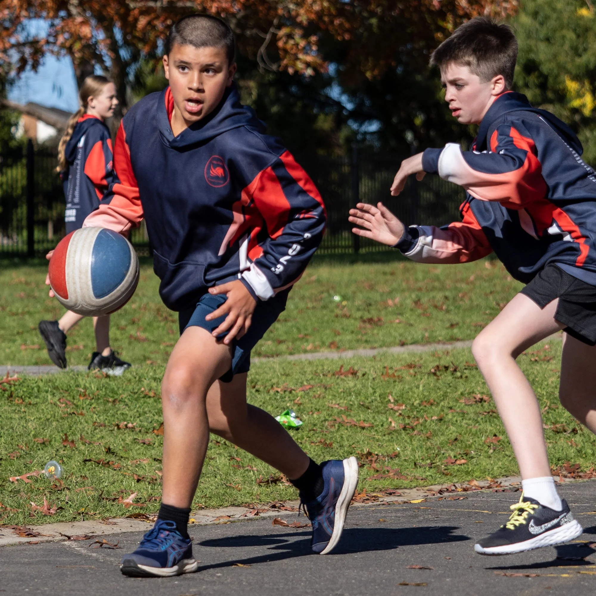 Two boys in athletic jackets playing street basketball outdoors, one dribbling a basketball, and the other preparing to defend.