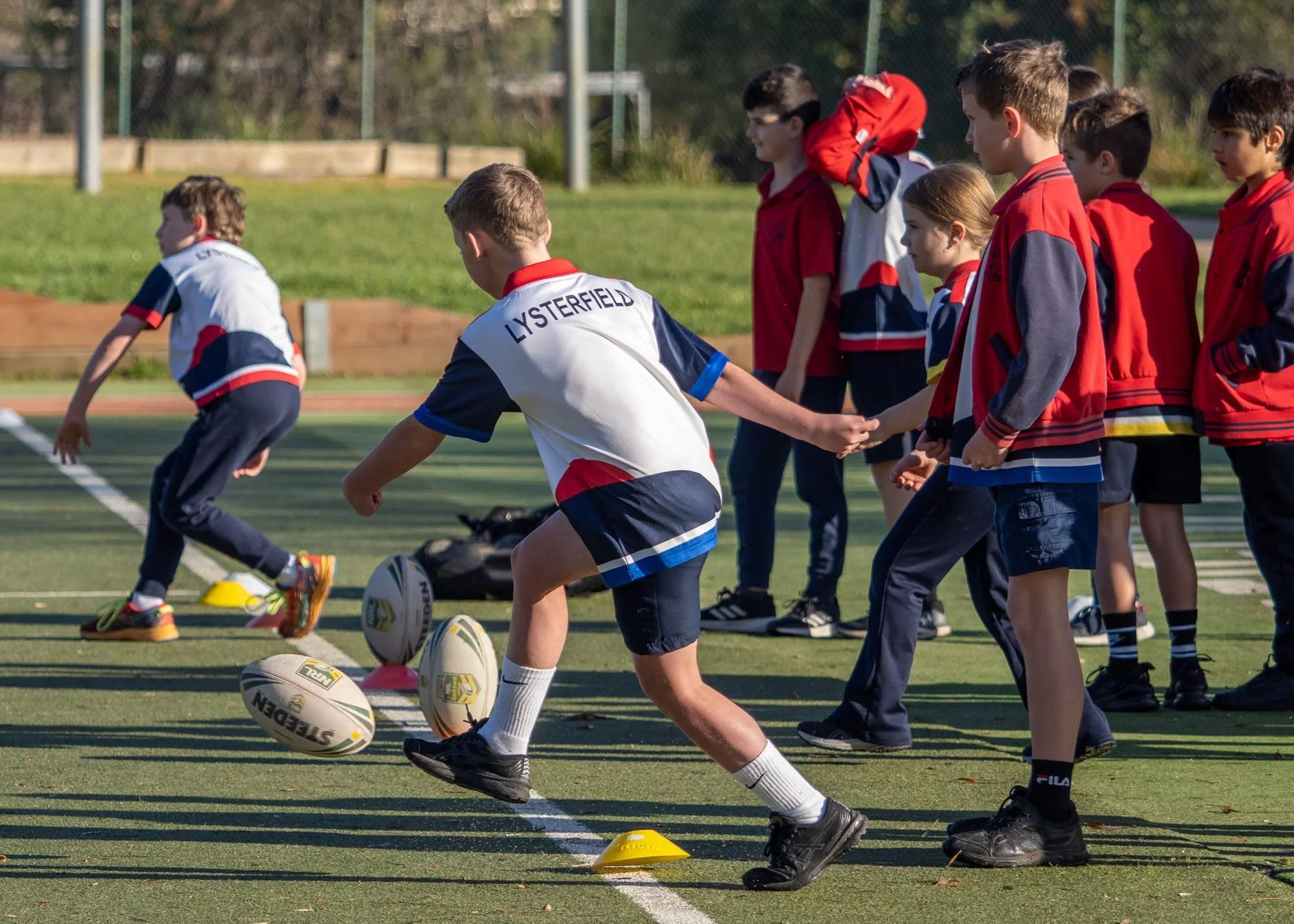 Group of children on a sports field participating in a rugby training session, wearing team uniforms.