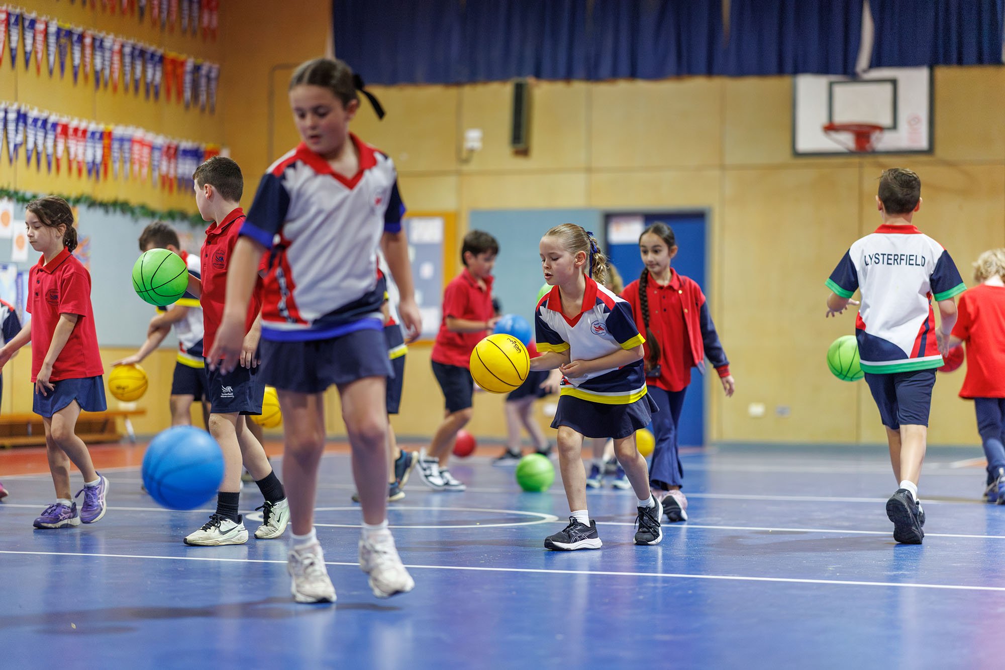 Children participating in a school gym class, playing with colorful balls on a blue gymnasium floor.