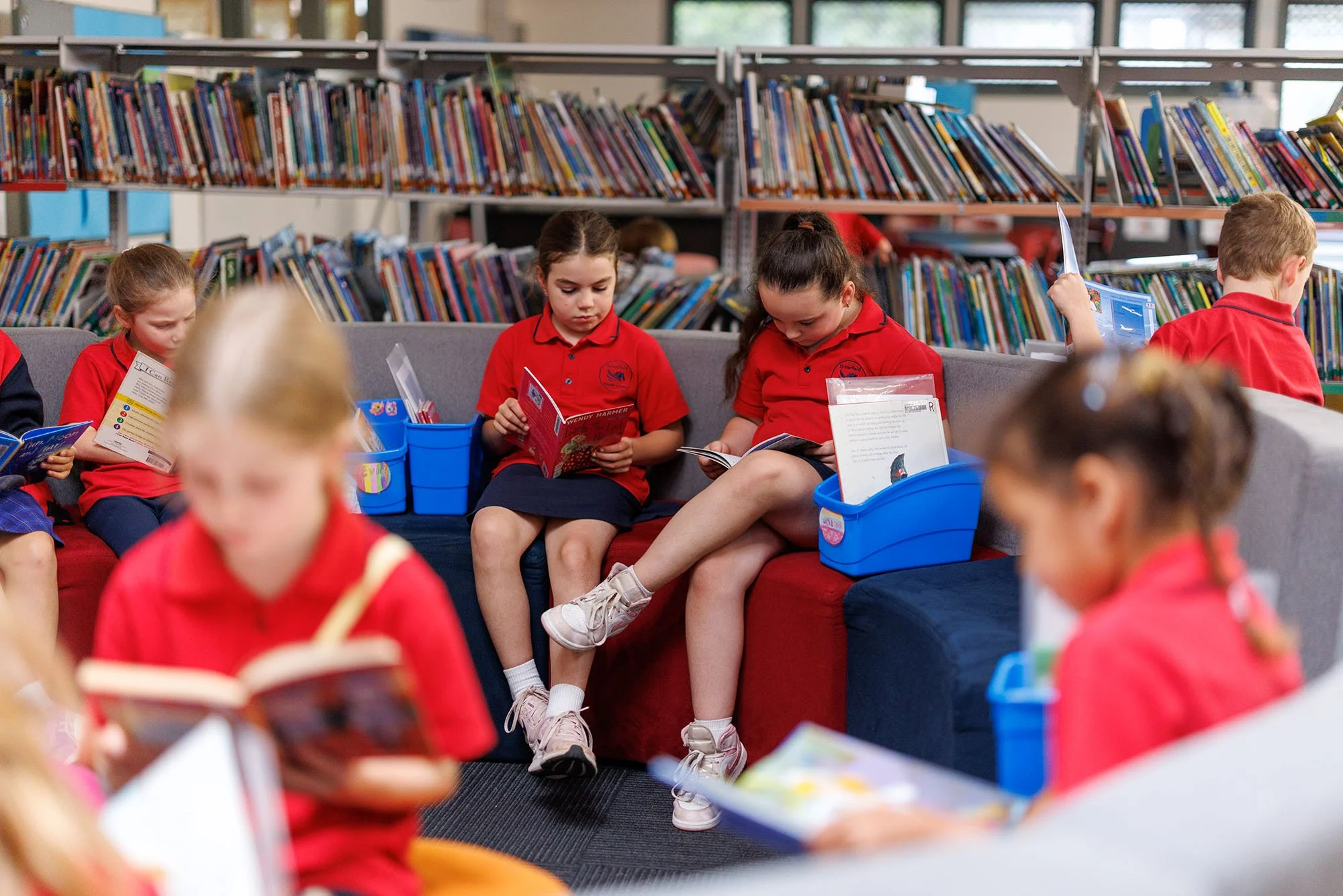 Children in red school uniforms reading books in a school library