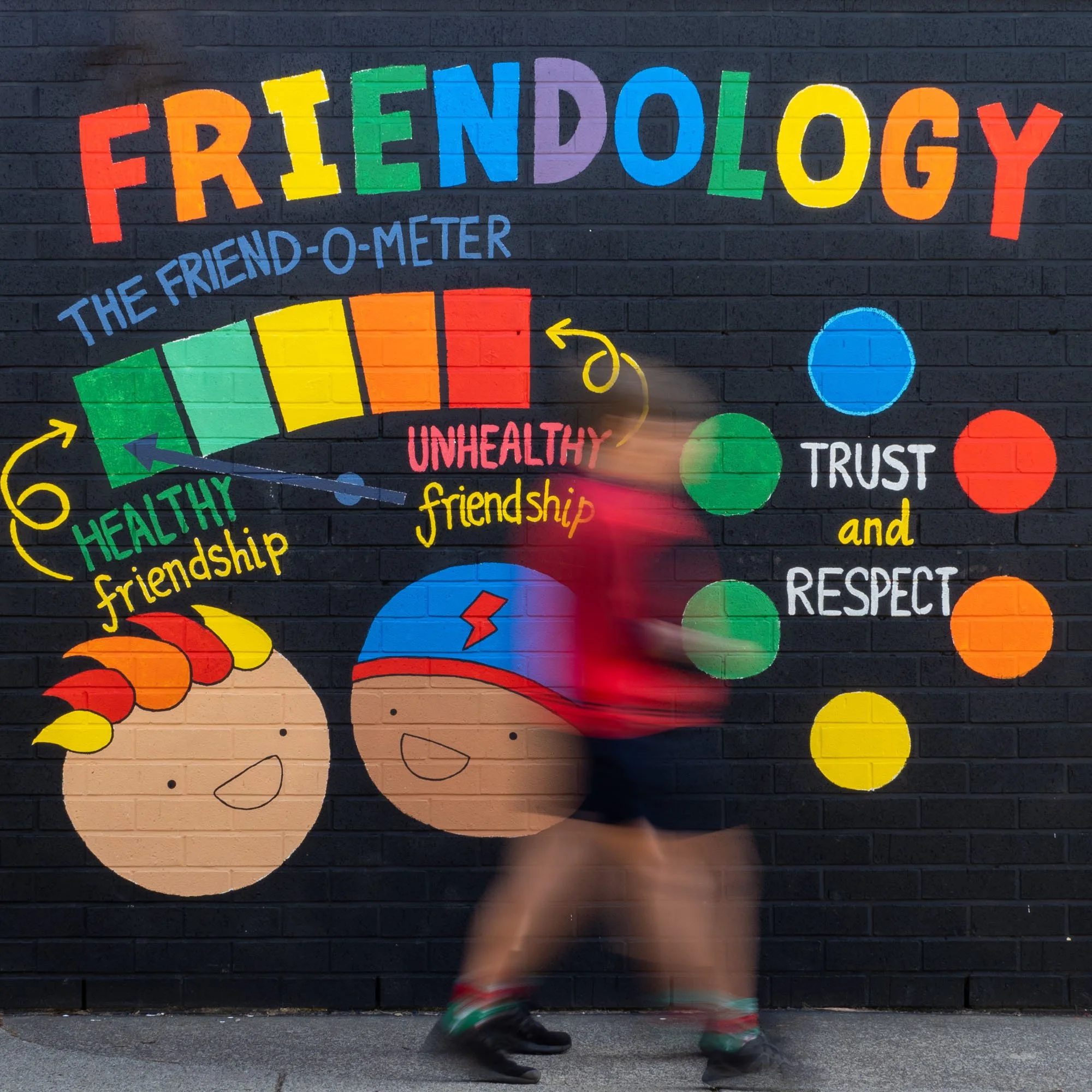 Colorful mural on a brick wall illustrating friendship with happy faces, rainbow-colored text, and a meter showing healthy and unhealthy friendship levels. Blue and green circles depict trust and respect.
