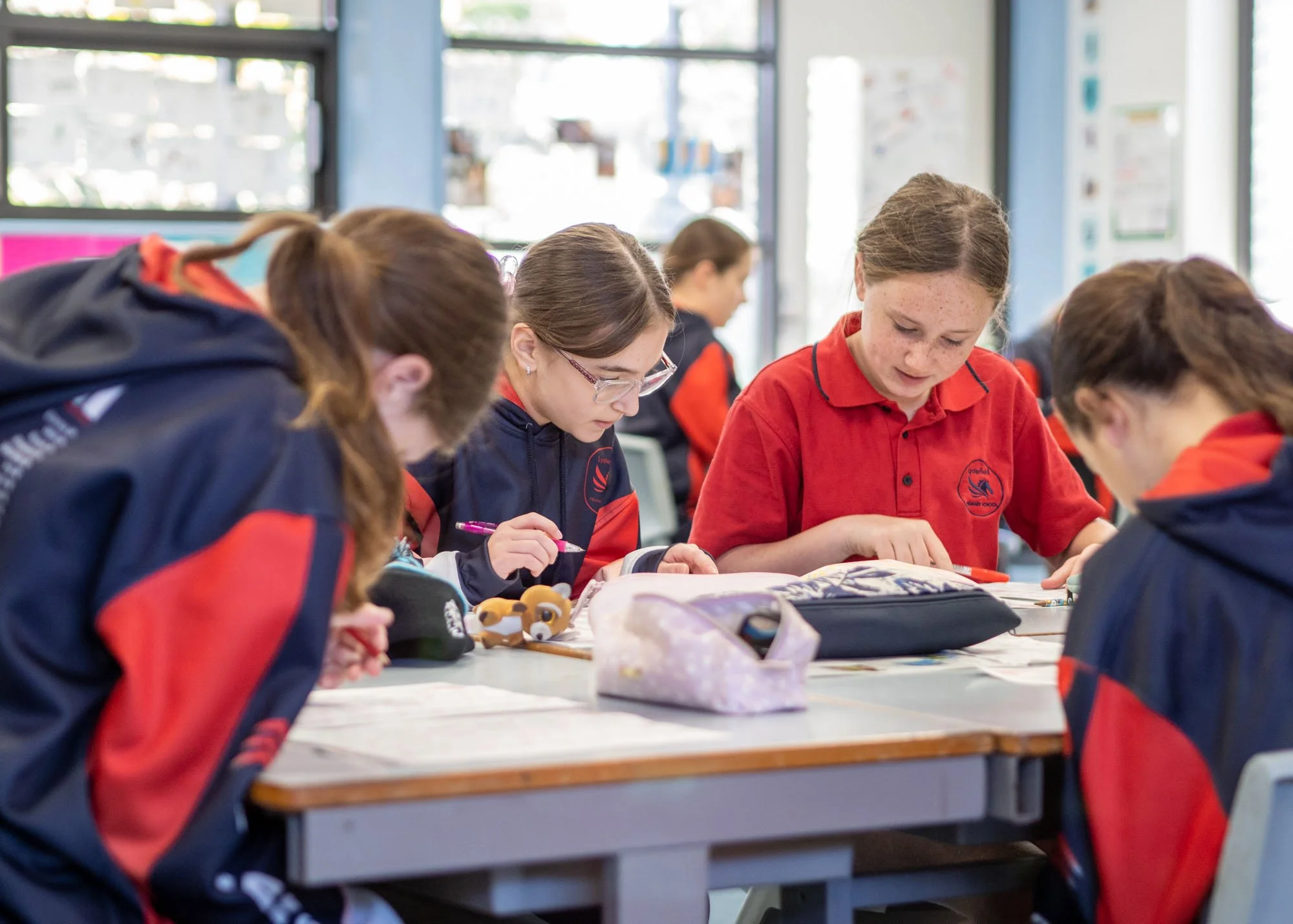Group of schoolgirls working together at a classroom table, focusing on their assignments.