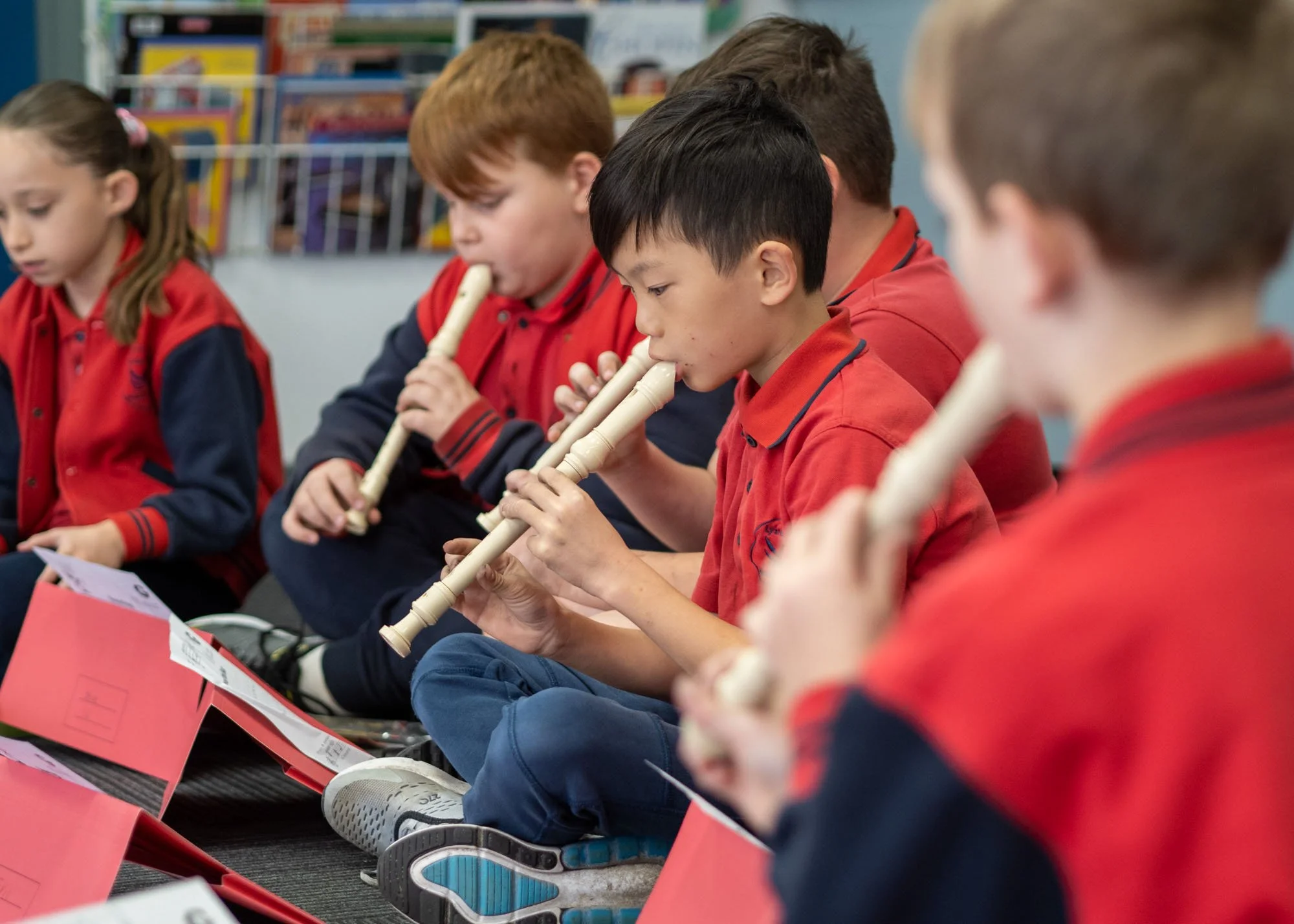 Children sitting on the floor in a classroom, playing recorders.