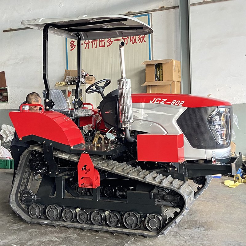 A small red and white tractor with tracked wheels, parked inside a warehouse or workshop.