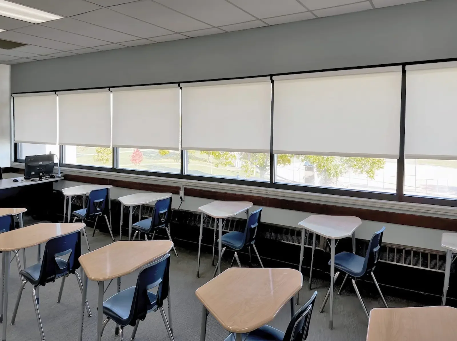 Clean light-filtering roller shades partially lowered installed in a classroom