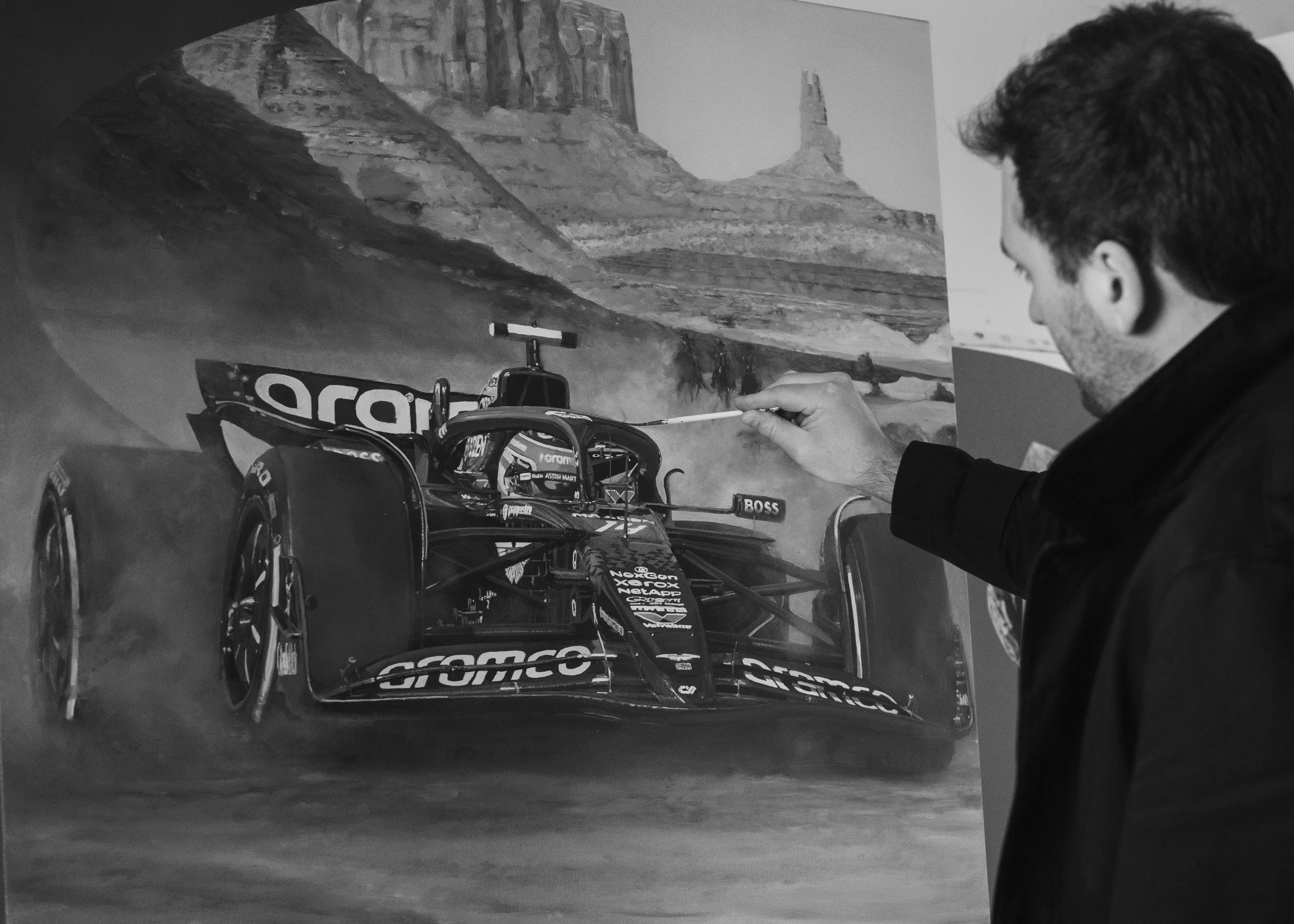 James Stevens painting a black and white mural of a race car on a wall, depicting a desert landscape with rock formations.