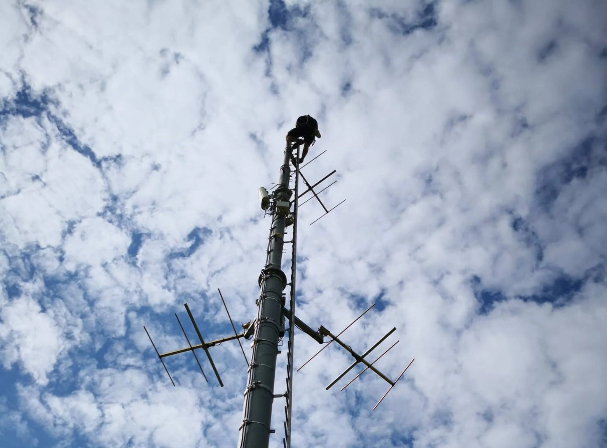 Ein Techniker arbeitet auf einem Funkmast gegen bewölkten Himmel.