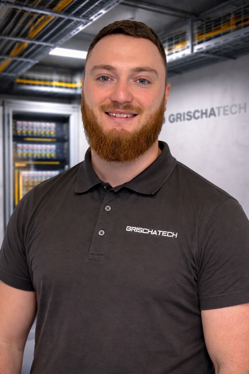 Mann in schwarzem Polo-Shirt mit Firmenlogo 'GRISCHATECH' vor Serverraum, lachend.