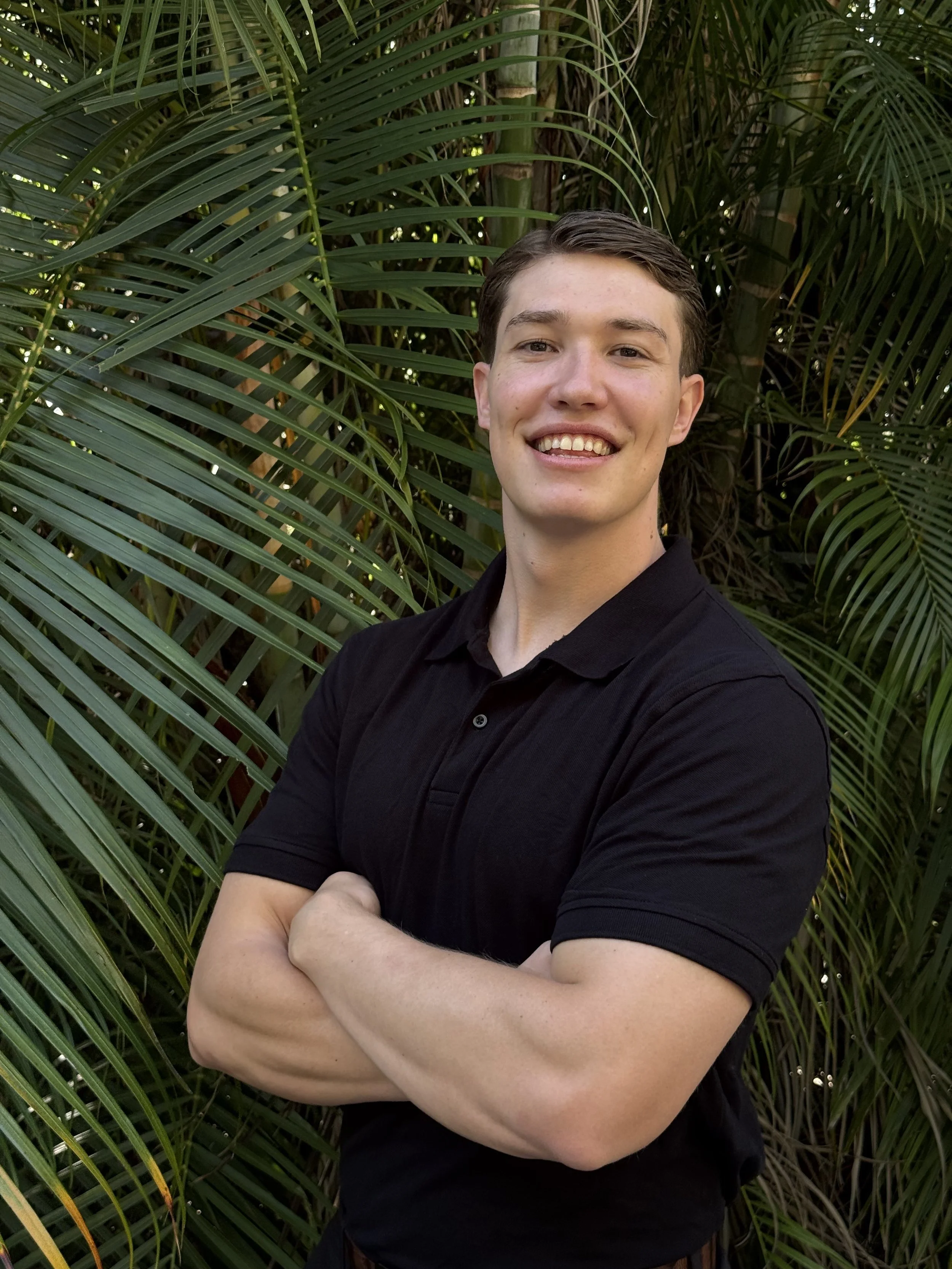 Joseph from Thrive Mobile Physio smiling in front of palm leaves.