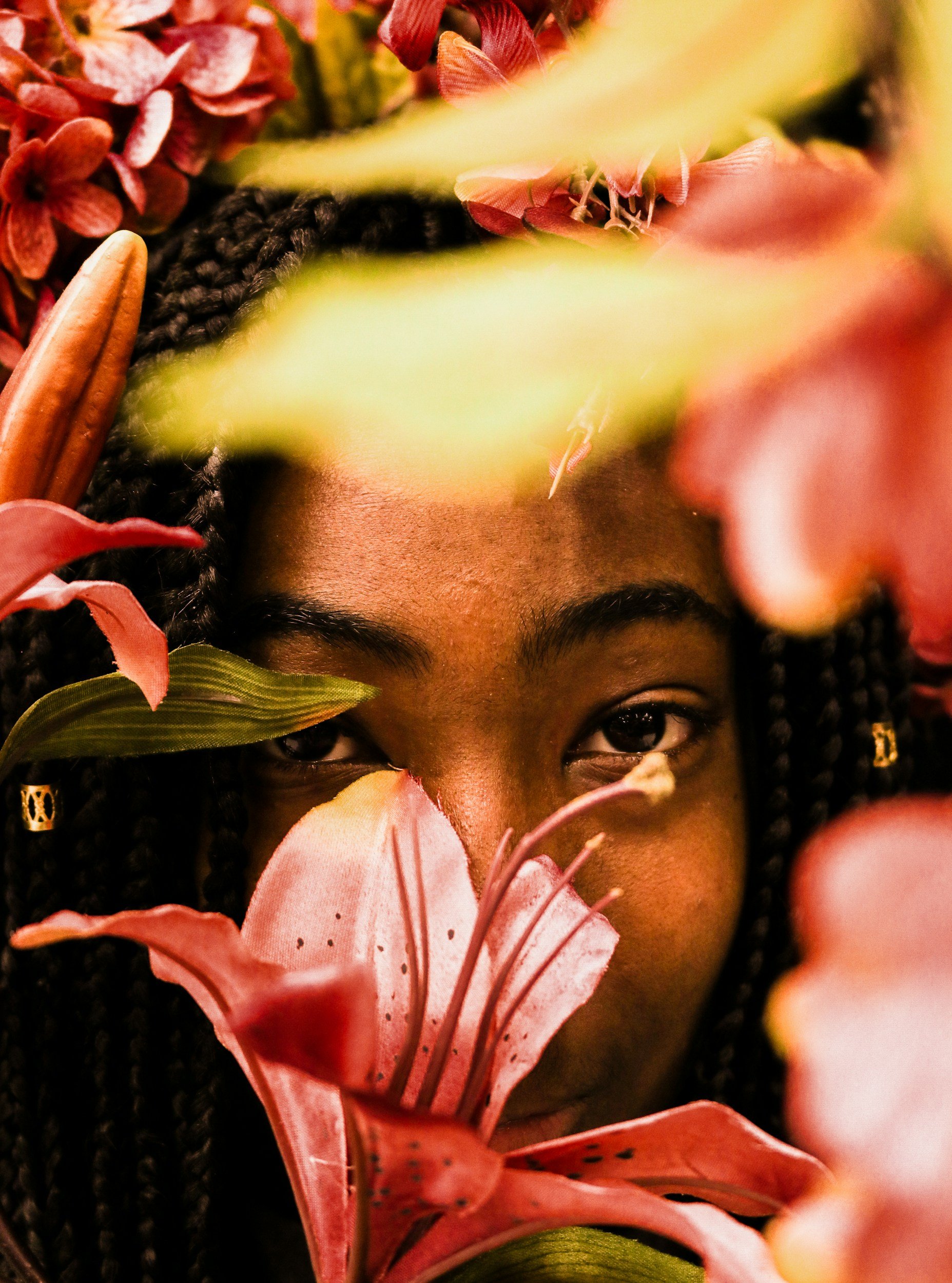 Close-up of a woman's face partially hidden behind pink lilies and other colorful flowers, with only her eyes visible.