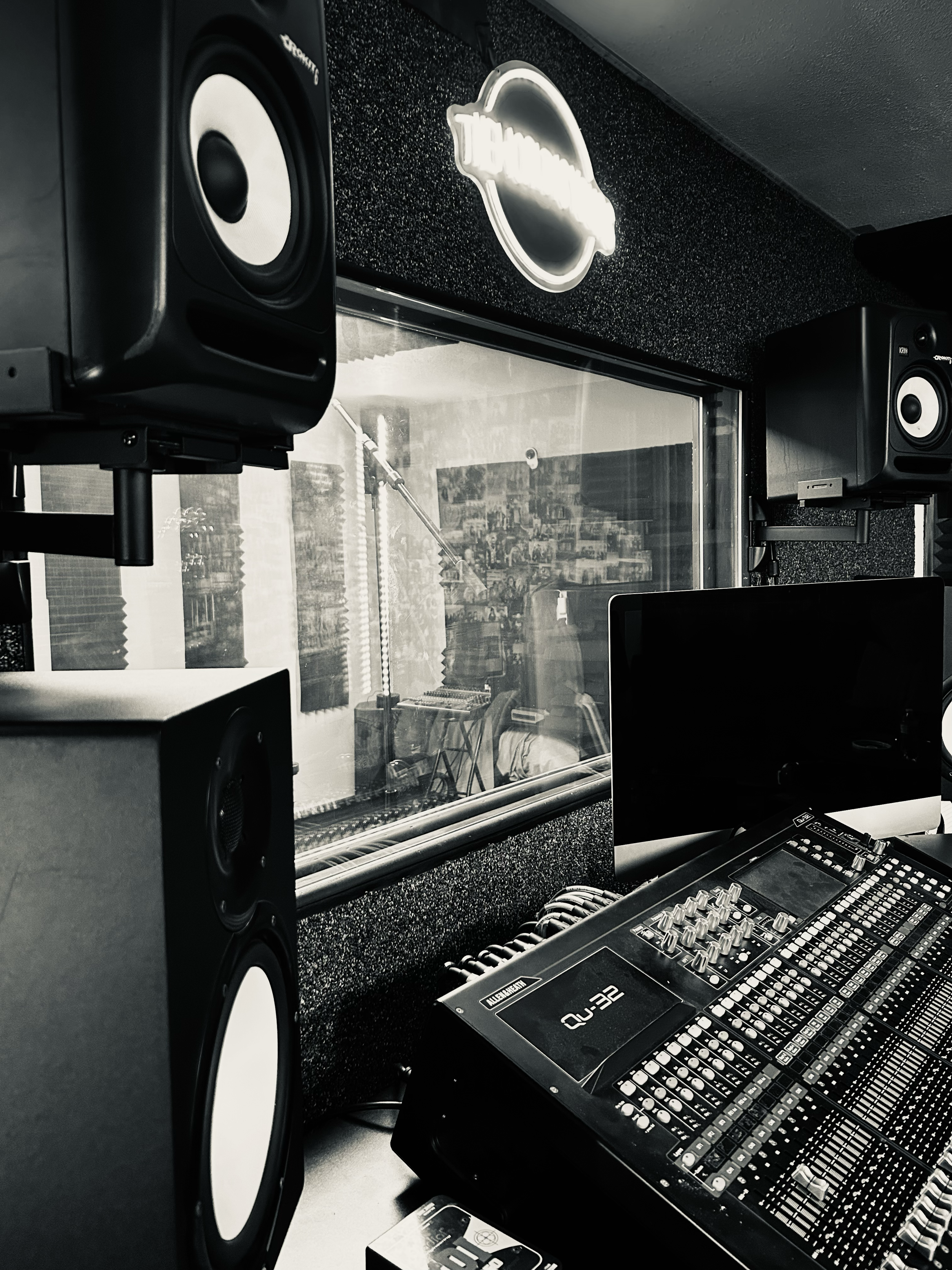 Sound recording studio with speakers, mixing console, and a window to an adjacent recording room.