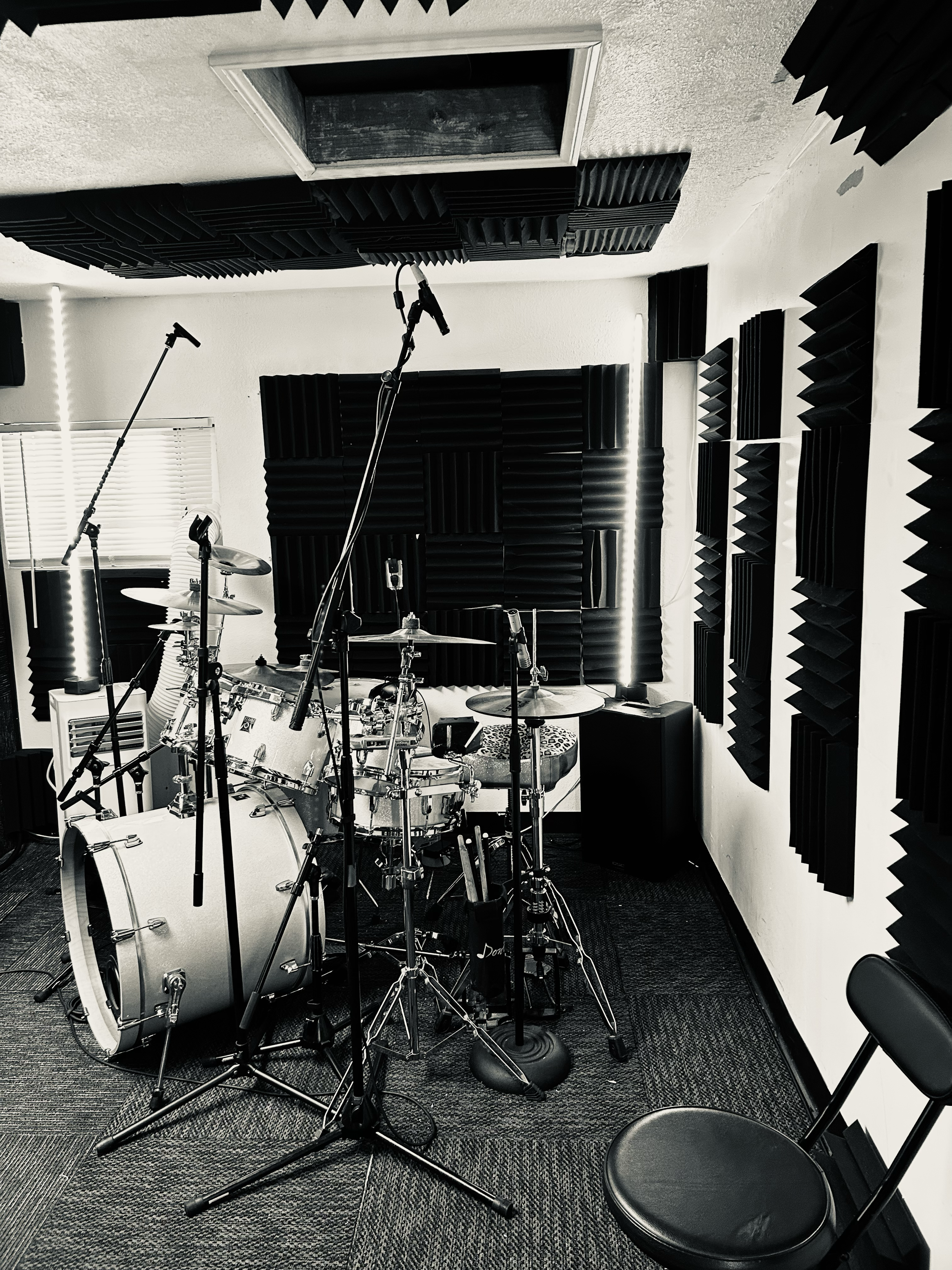 Music recording studio with drum set, microphone stands, and soundproofing foam panels on the walls.