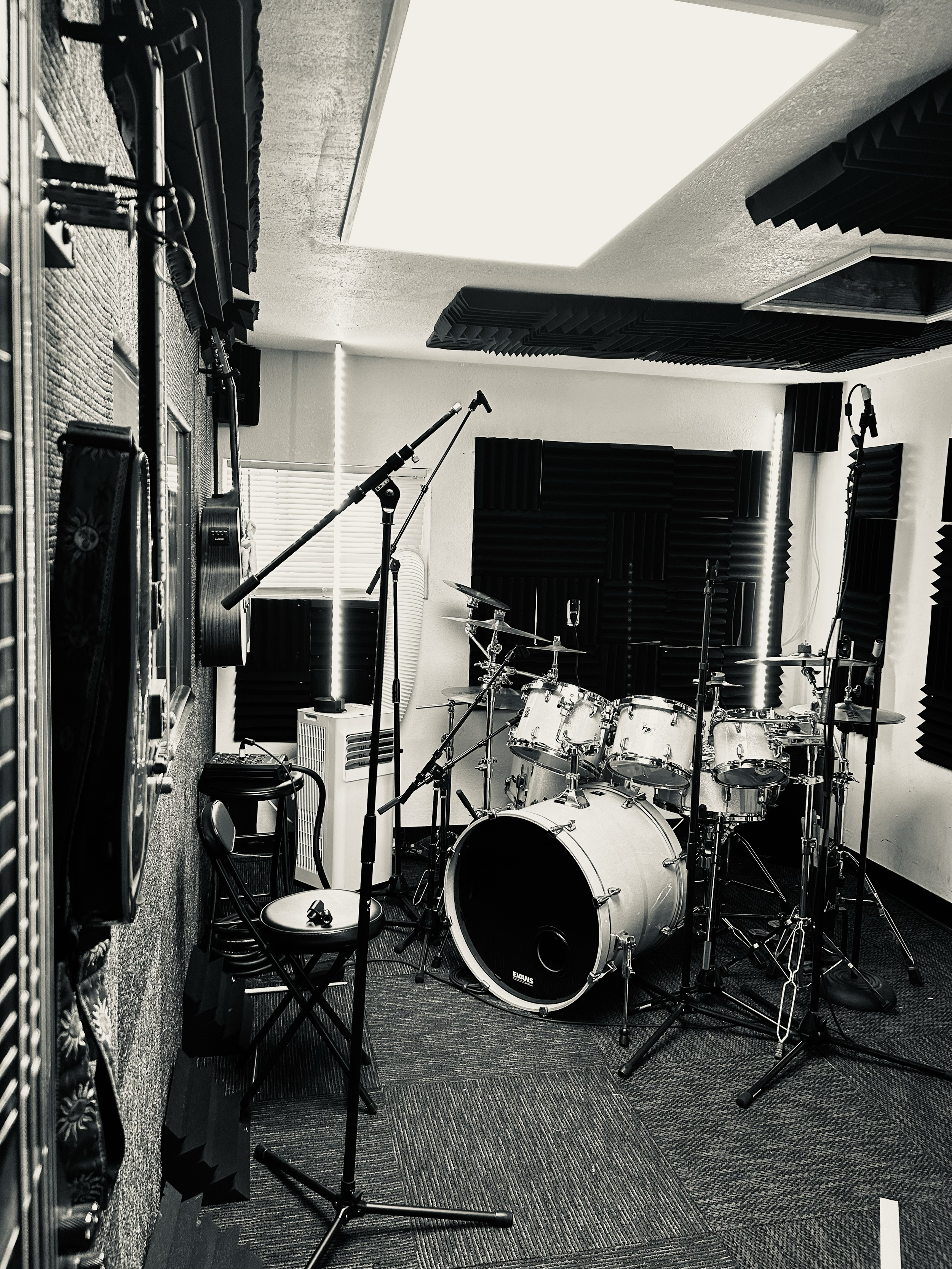 A music recording studio with a drum set, microphone, acoustic foam panels on the walls, and soundproofing elements on the ceiling.