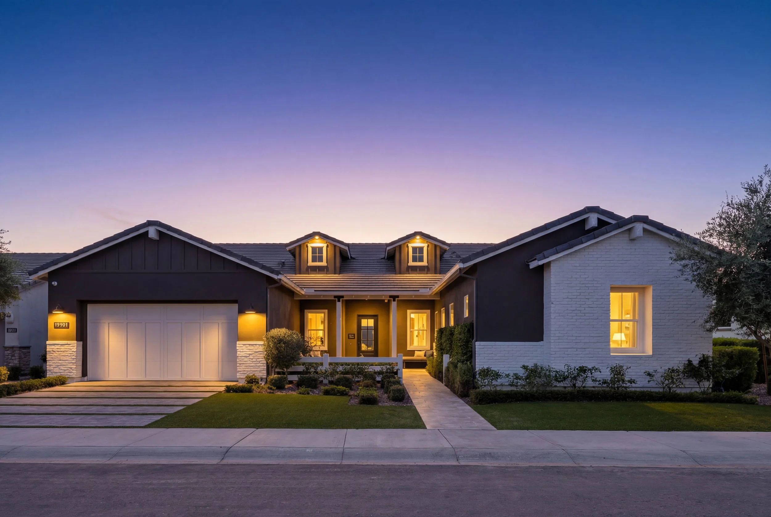Modern single-story house with a white brick exterior and black accents, illuminated at dusk, with a well-manicured yard and driveway.
