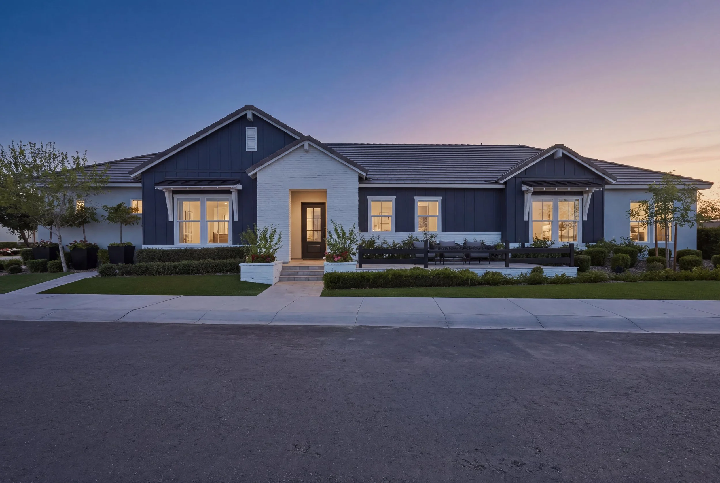 Modern single-family house with white and dark blue exterior, front porch, and landscaped yard during sunset.