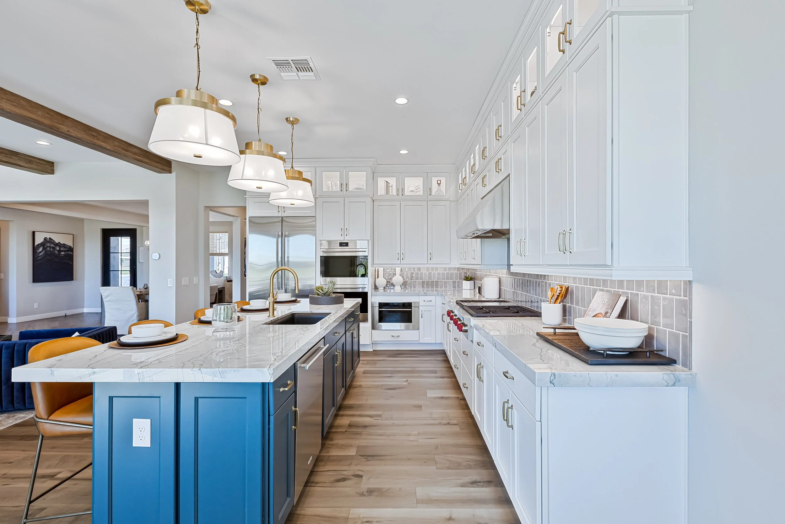 Modern kitchen with white cabinets, a blue island, and gold accents, featuring pendant lighting, a marble countertop island, and stainless steel appliances.