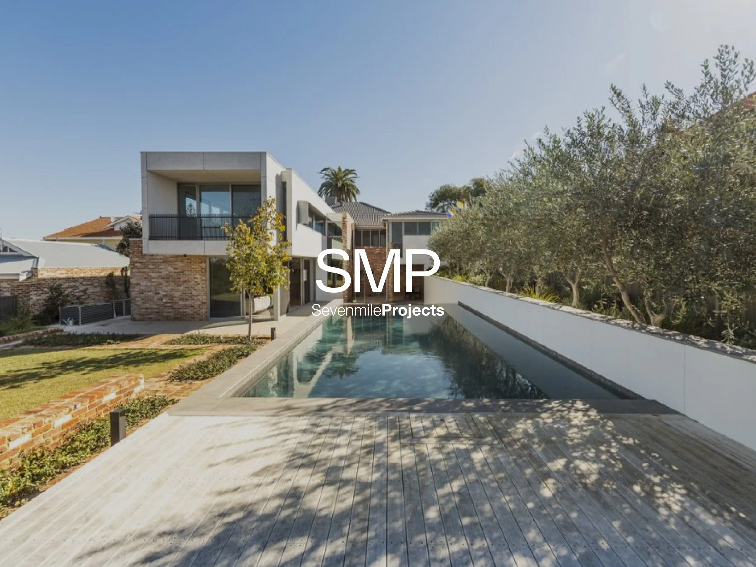Modern house with a swimming pool, surrounded by trees and greenery, under a clear blue sky.