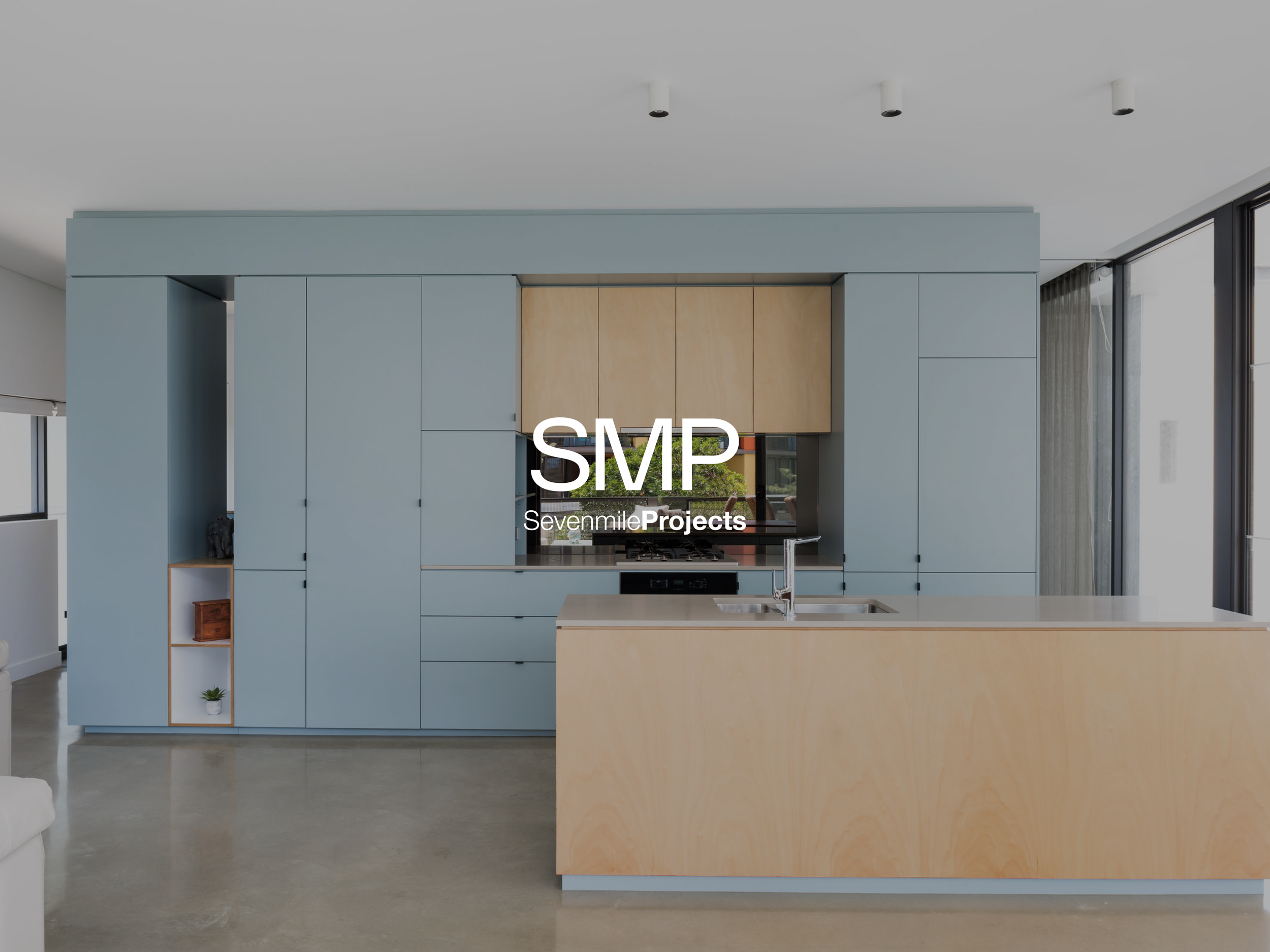 Modern kitchen with blue cabinets and a light wood island, stainless steel sink, and large glass windows.